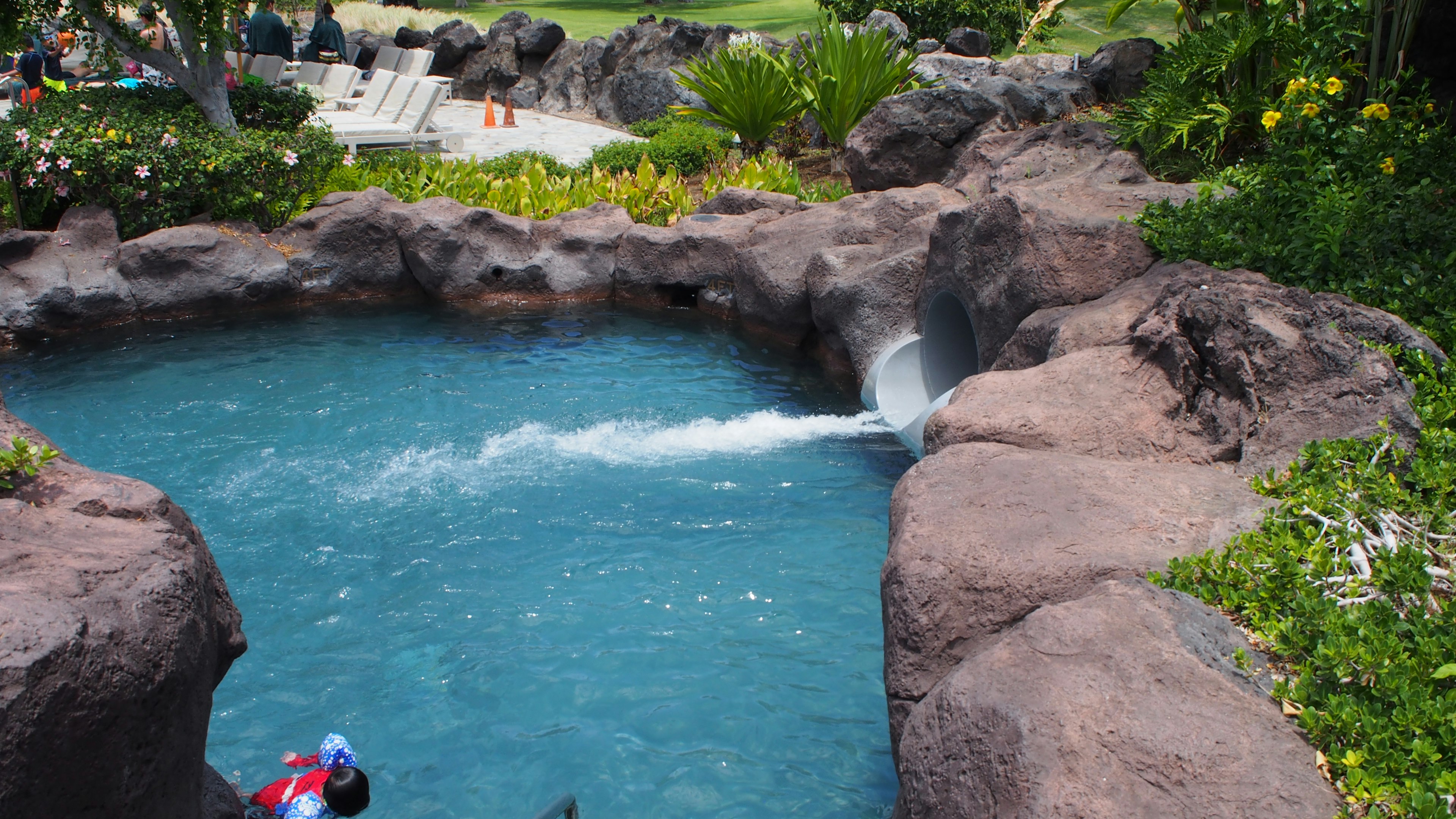 Resort pool with turquoise water surrounded by rocks and lush greenery