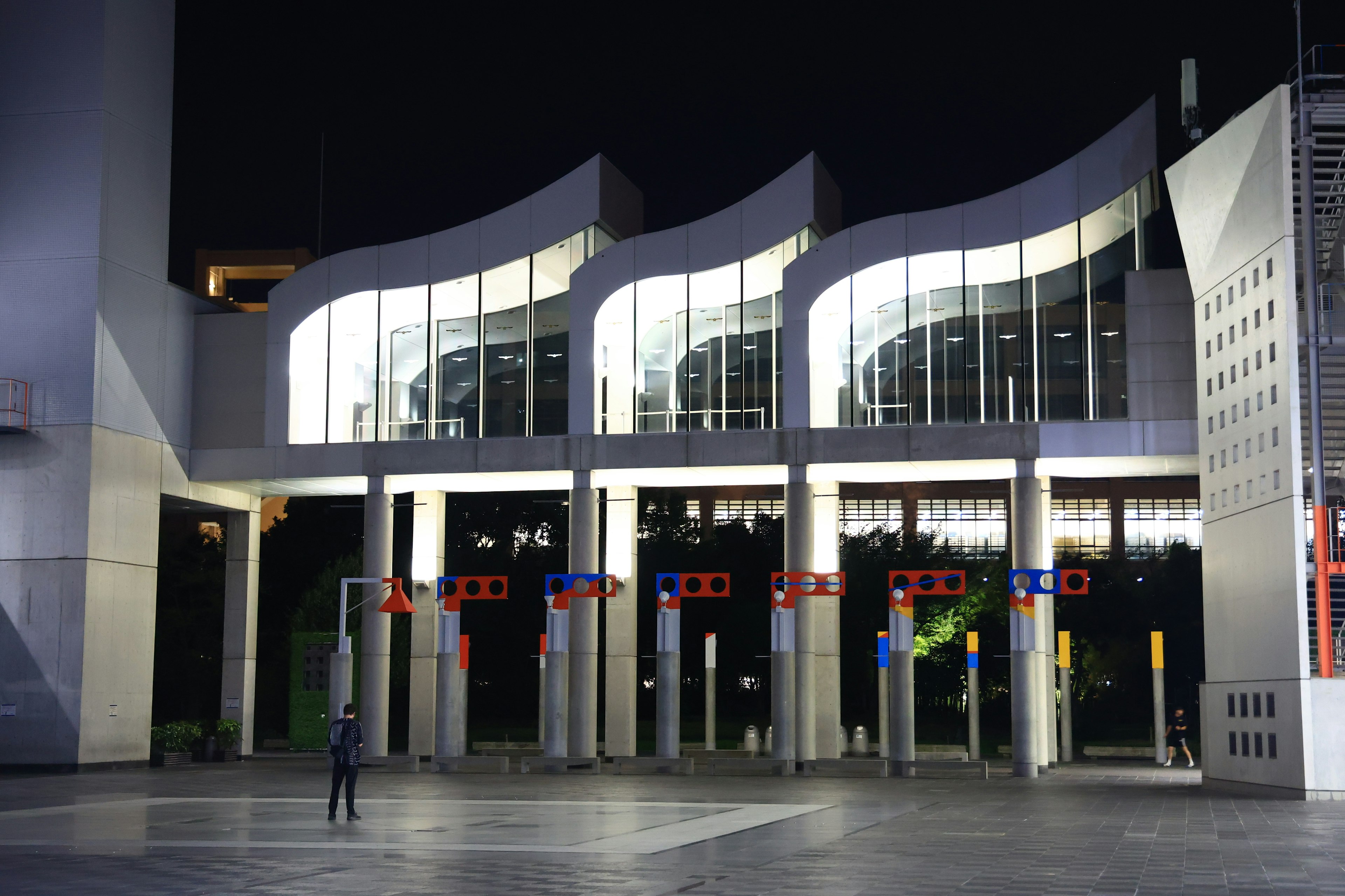 Façade d'un bâtiment moderne la nuit avec un toit ondulé et un éclairage lumineux