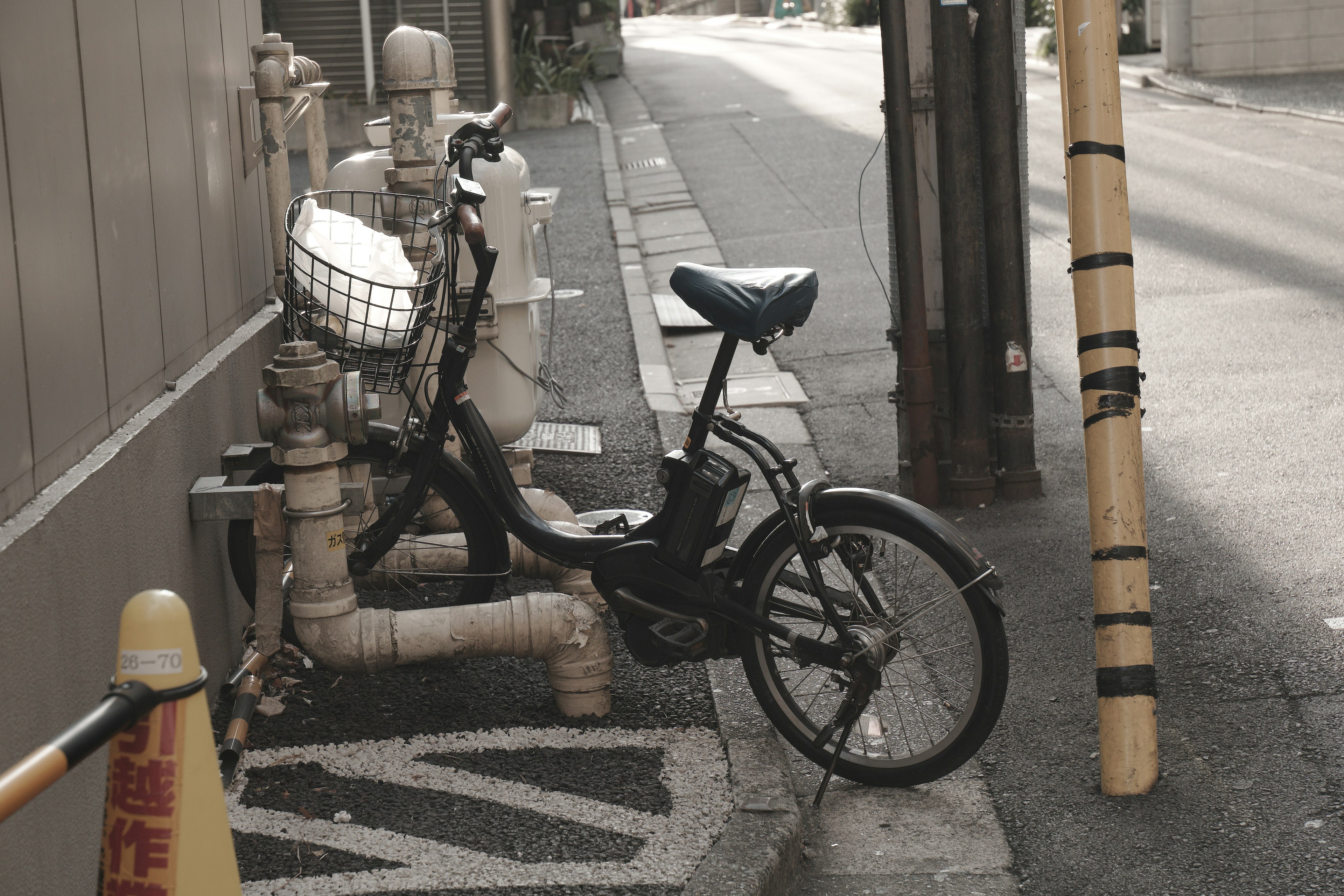 A bicycle parked next to a water pipe in a narrow alley