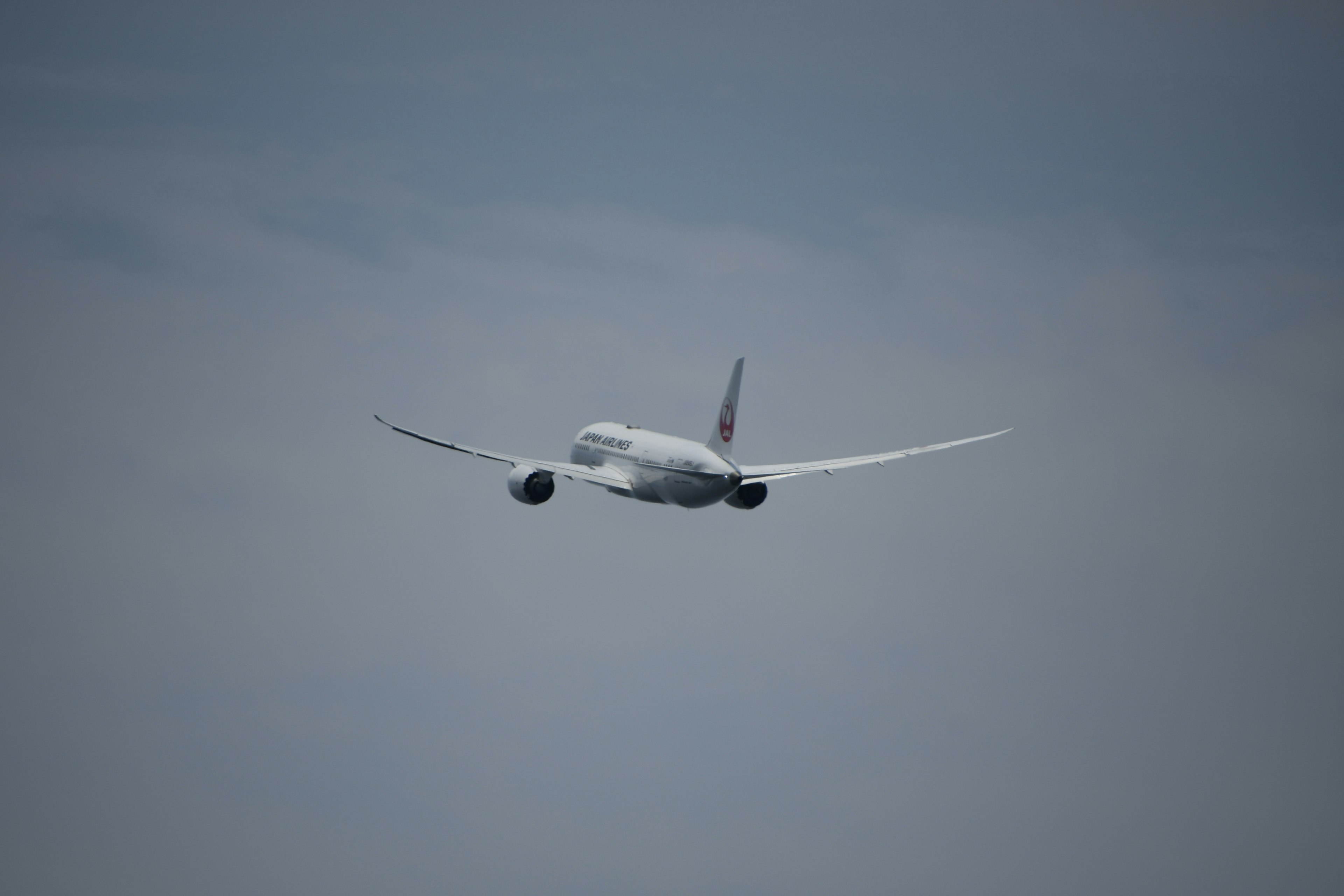 空を飛ぶ航空機の後ろ姿と青い空