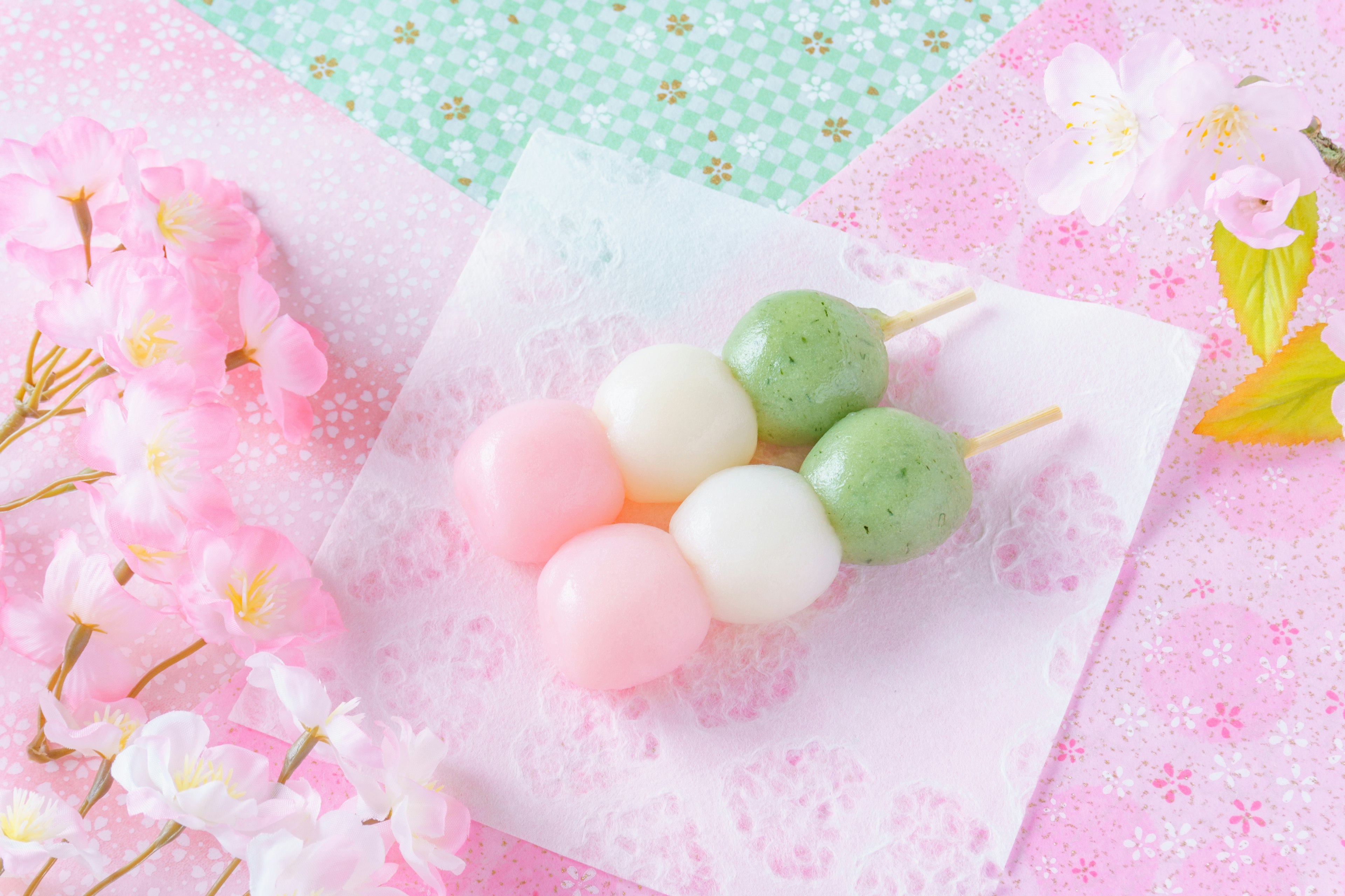 Dango tiga warna di piring putih dengan bunga sakura dan latar belakang merah muda