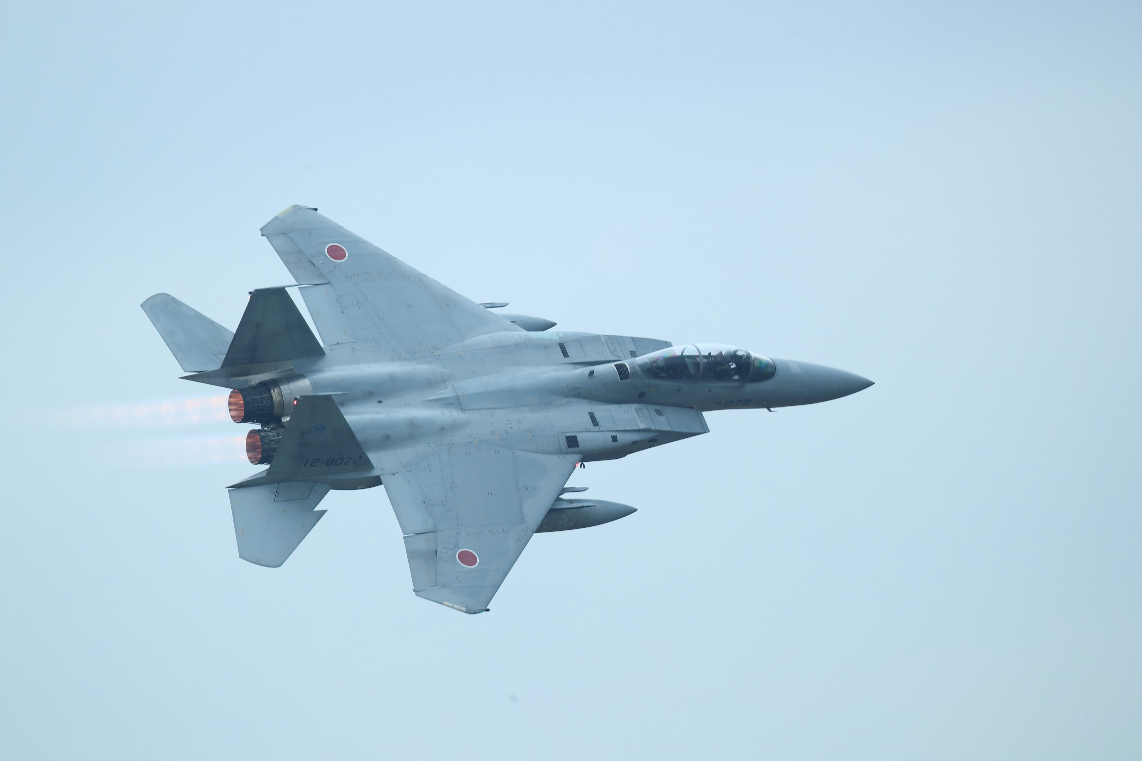 Japanese F-15 fighter jet flying in the sky with smoke trailing from the engines