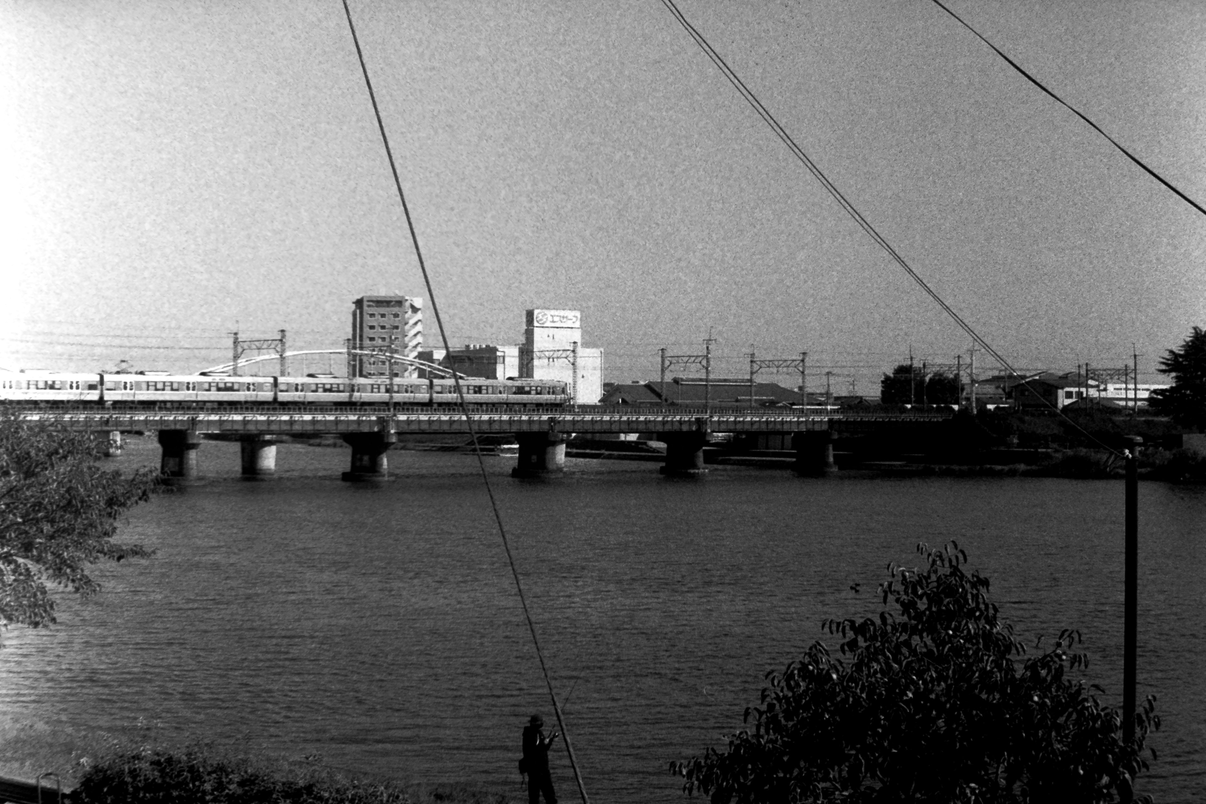 Imagen en blanco y negro de un puente sobre un río con edificios y vías de tren