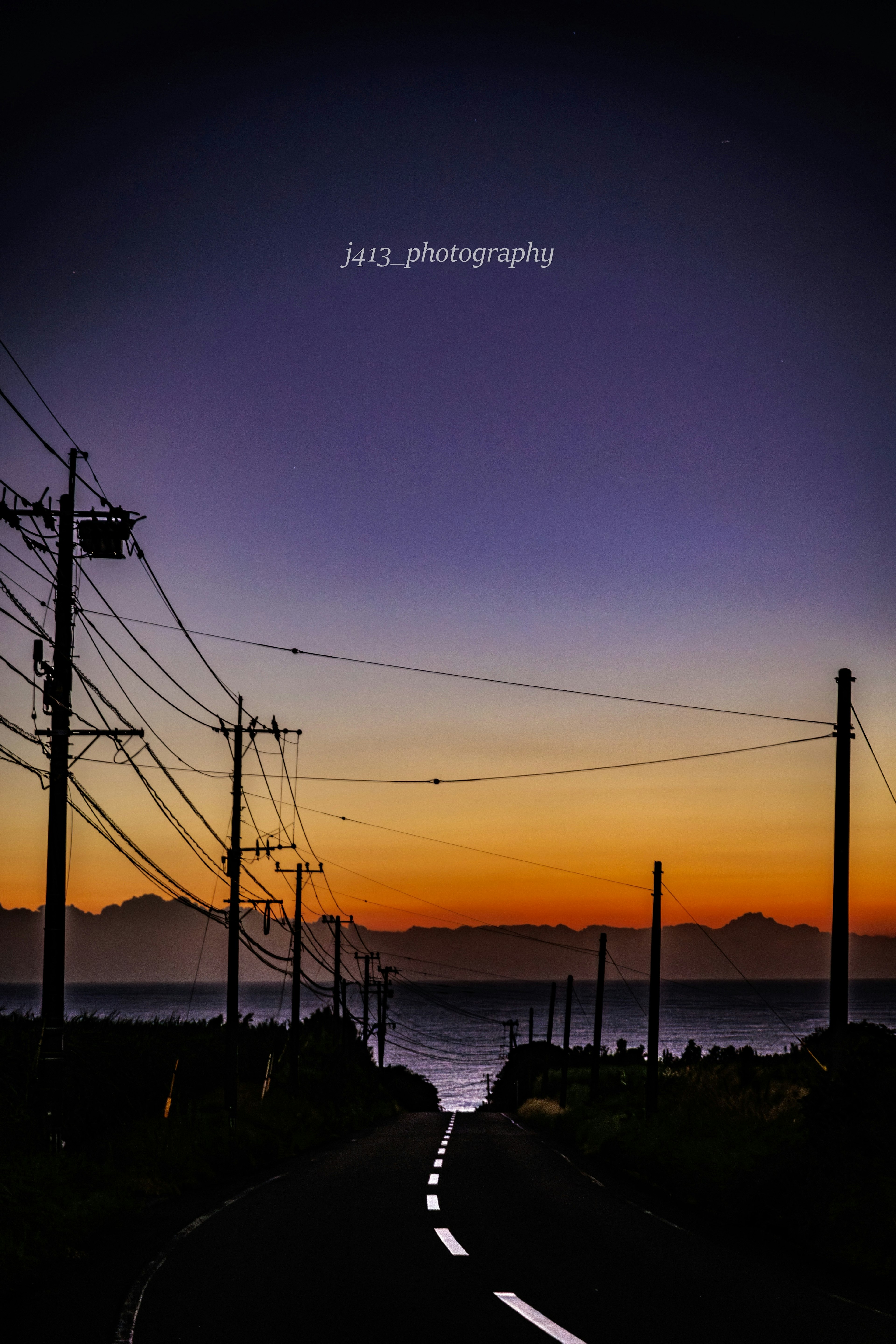 Strada panoramica che conduce al mare al crepuscolo con linee elettriche e un cielo arancione e viola mozzafiato