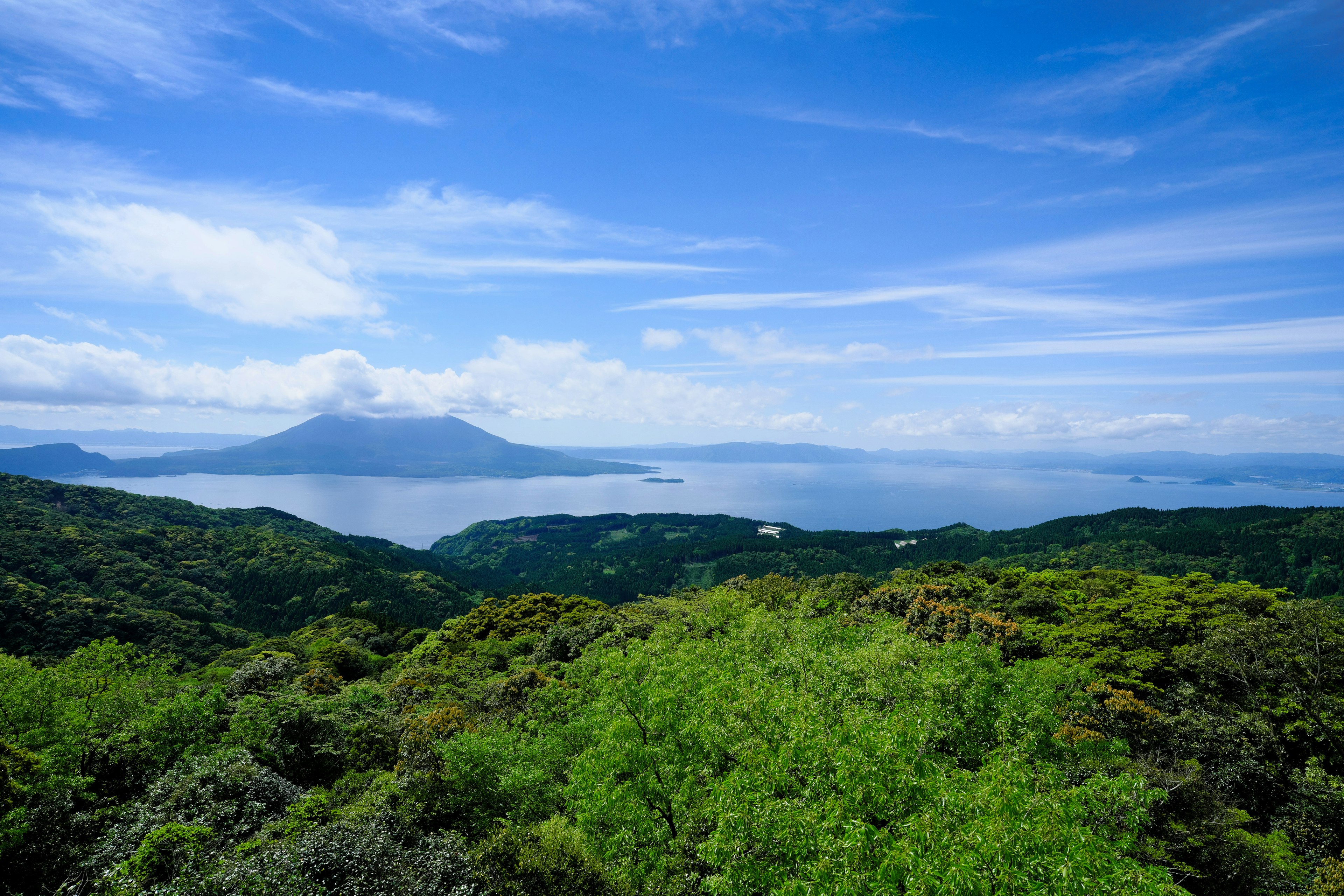 Vista panoramica di colline verdi sotto un cielo blu con oceano e isola in lontananza