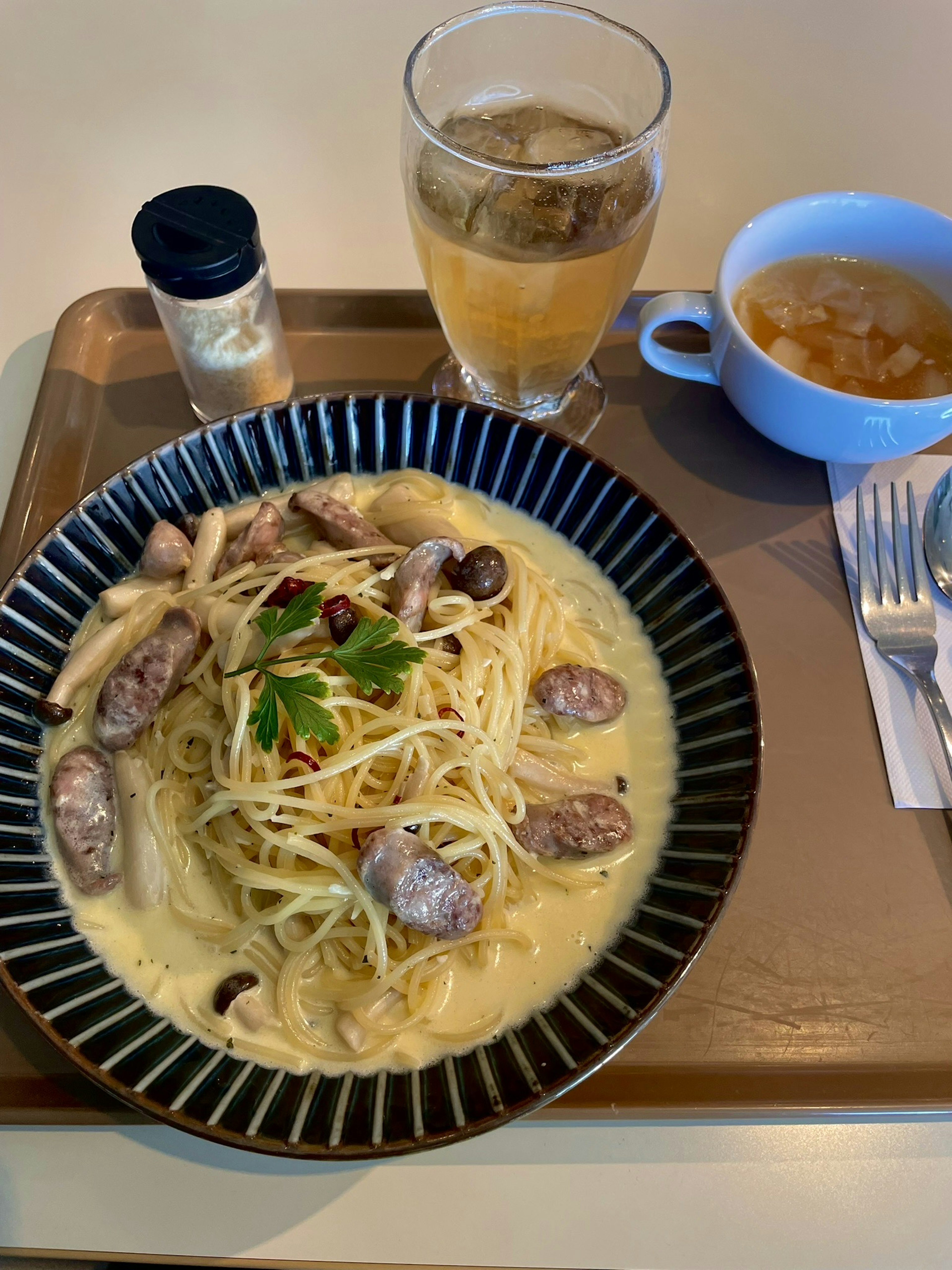 A plate of pasta with sausage garnished with parsley served alongside a drink and soup