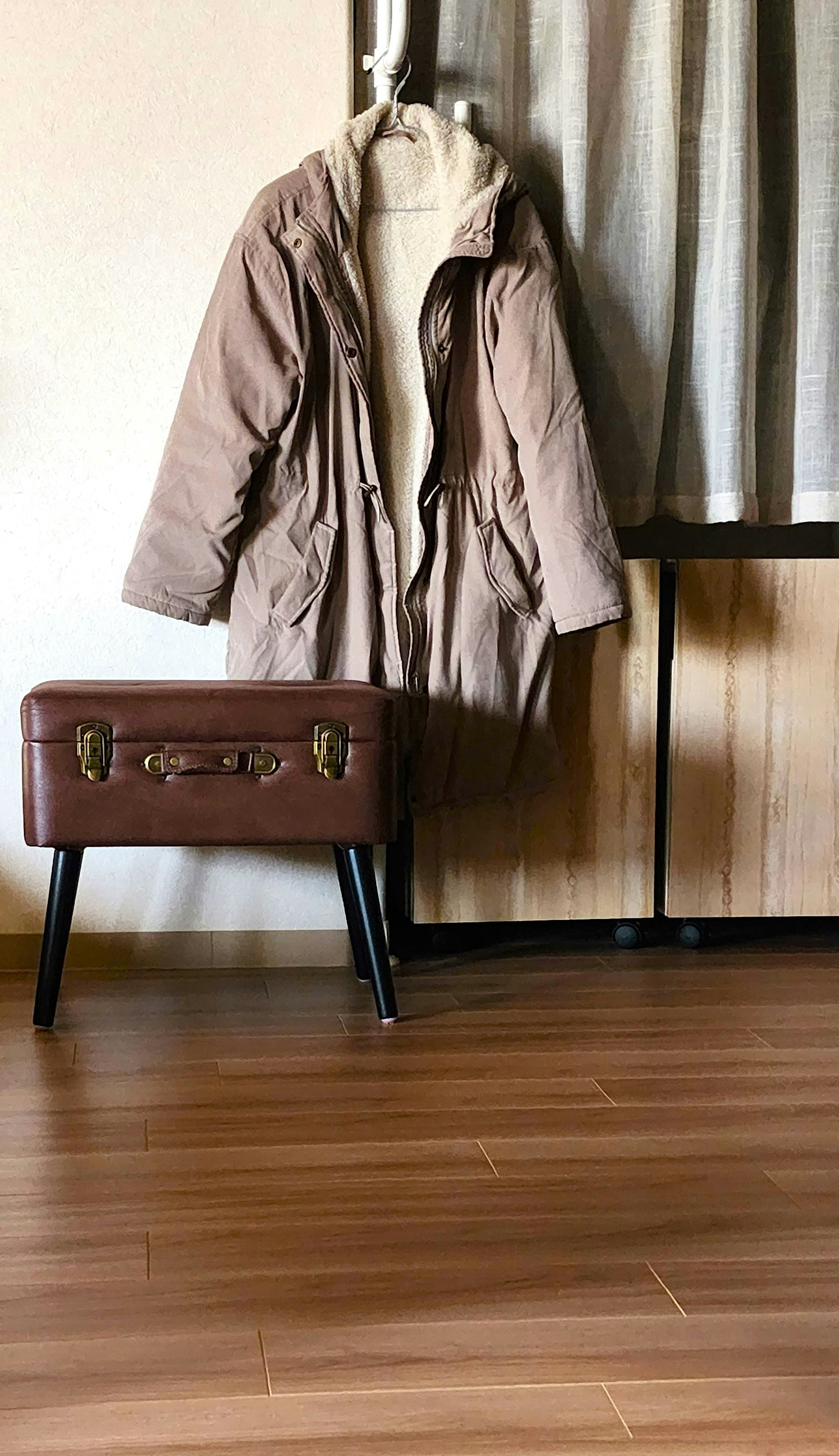 A warm brown coat hanging on a hanger in a simple indoor setting