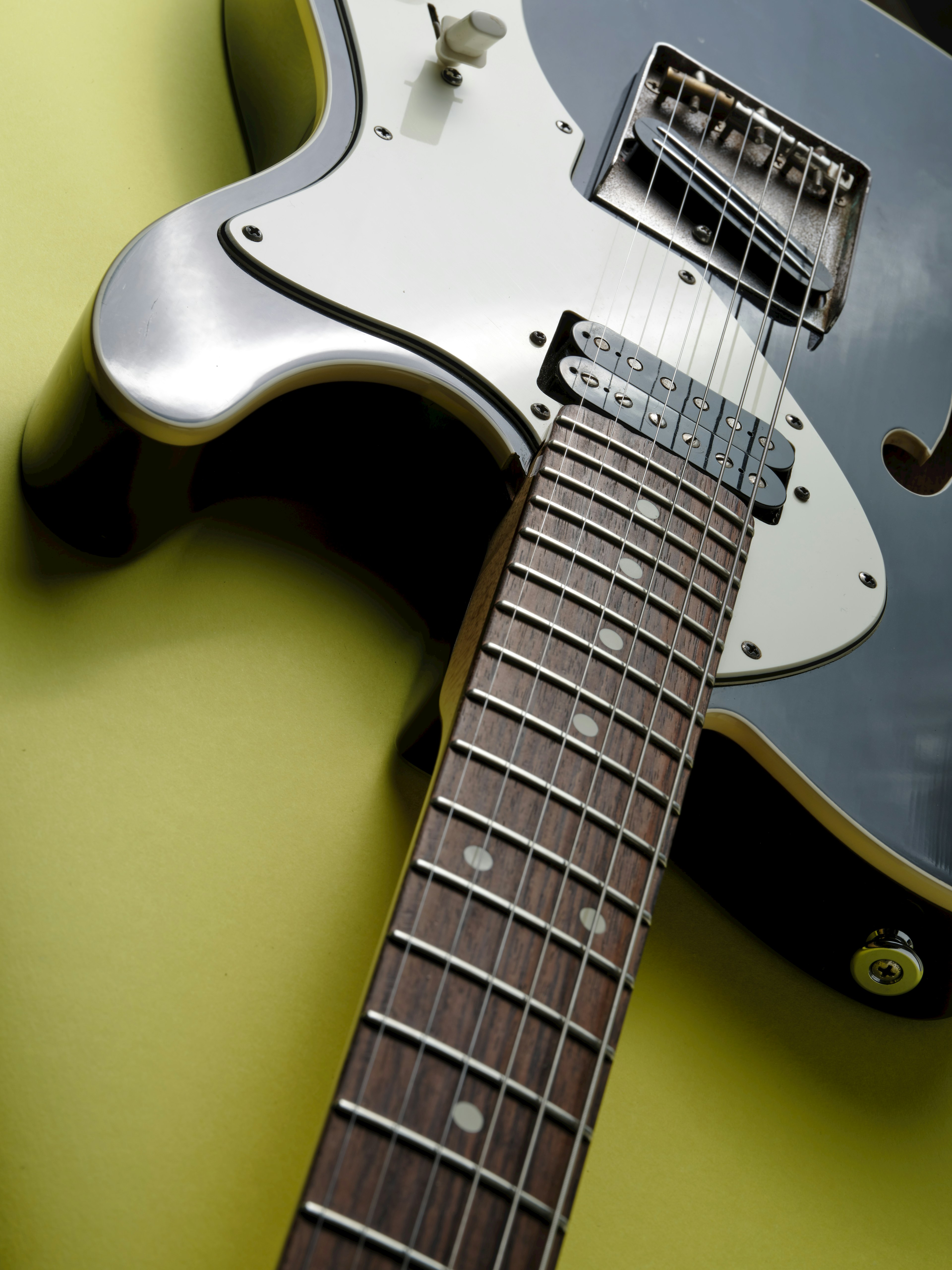 Close-up of a black electric guitar with a wooden neck and visible guitar pickup