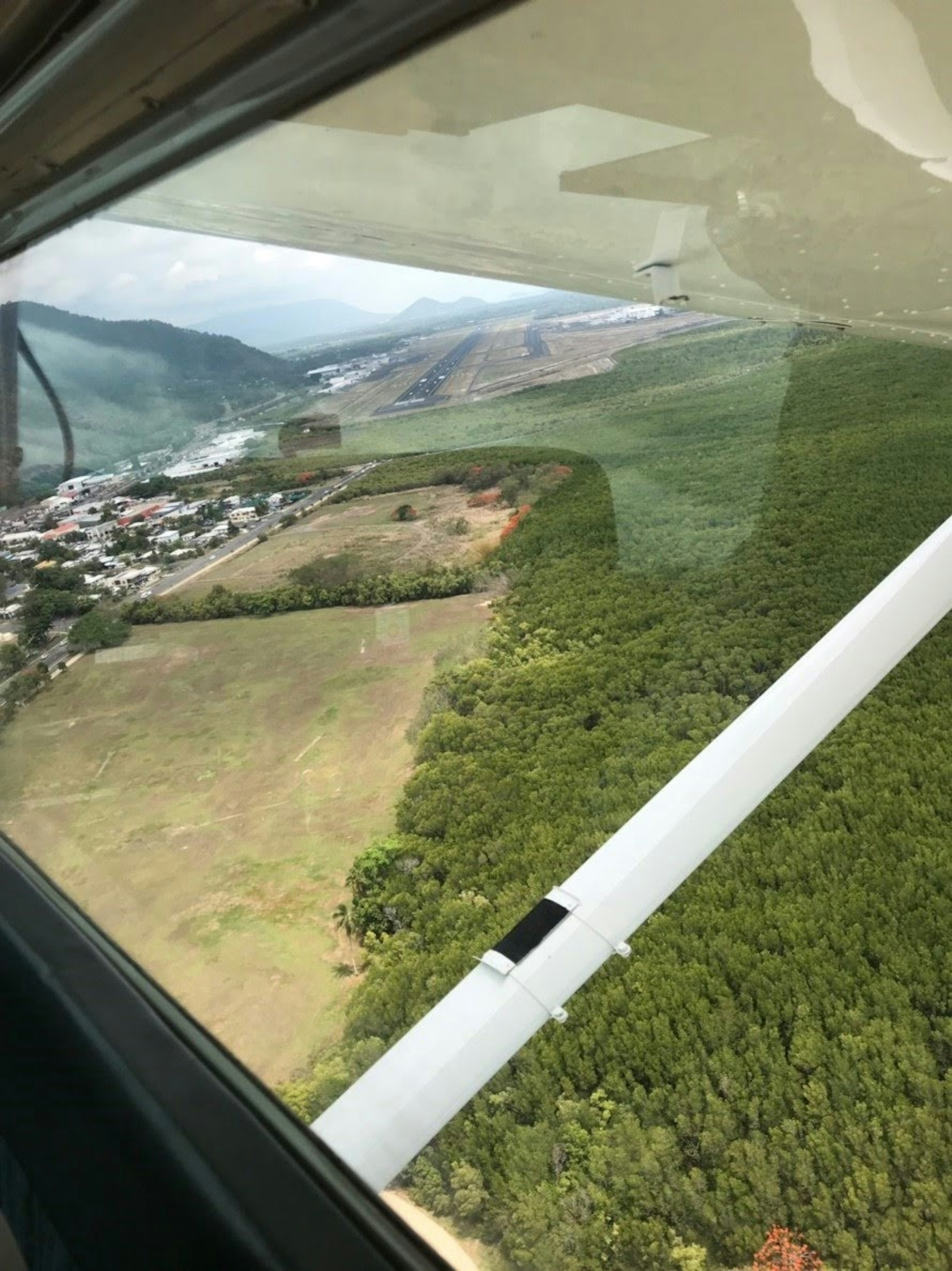 Vista aérea desde una ventana de avión que muestra vegetación exuberante y una ciudad cercana