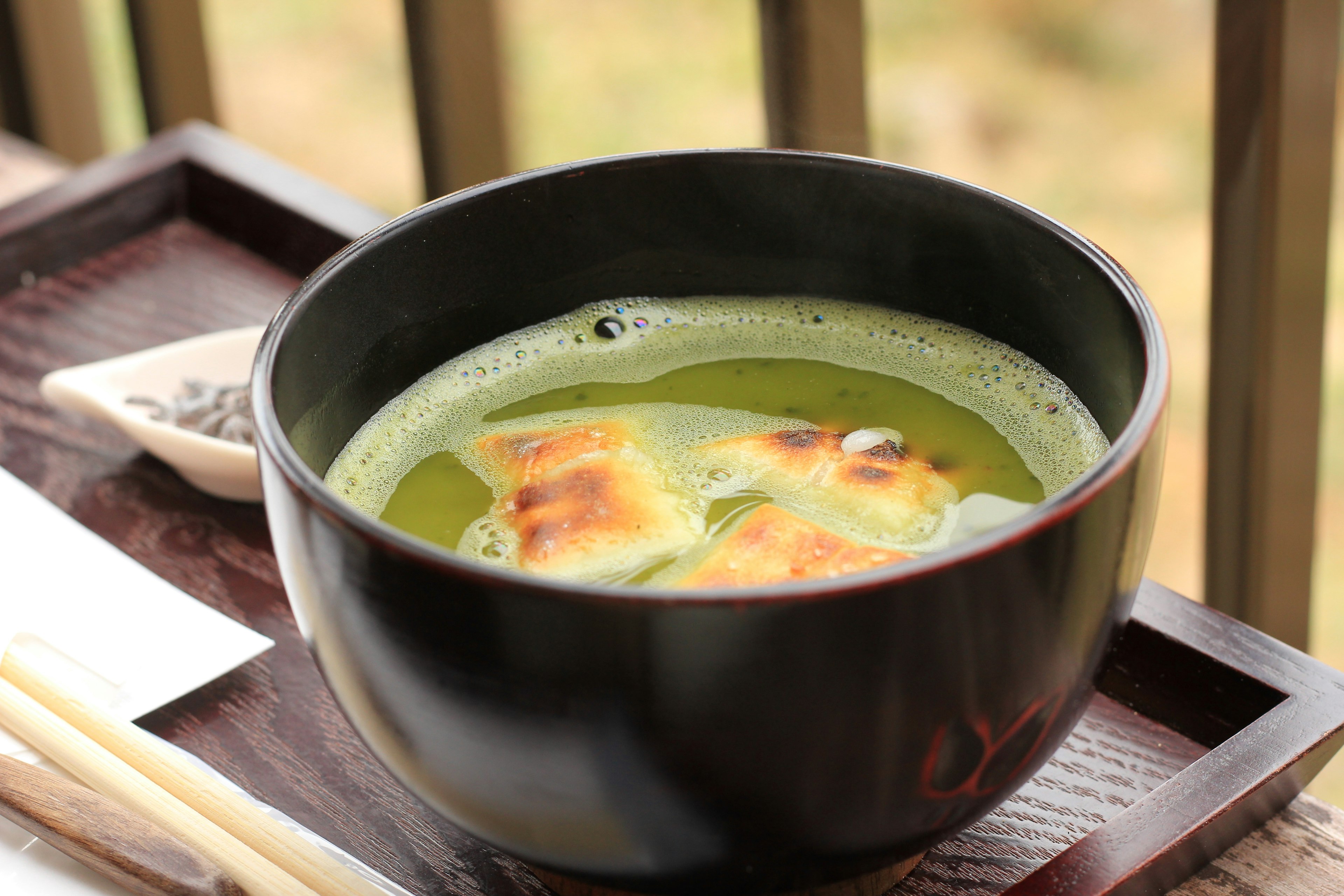 A black bowl containing green tea soup with grilled rice cakes floating