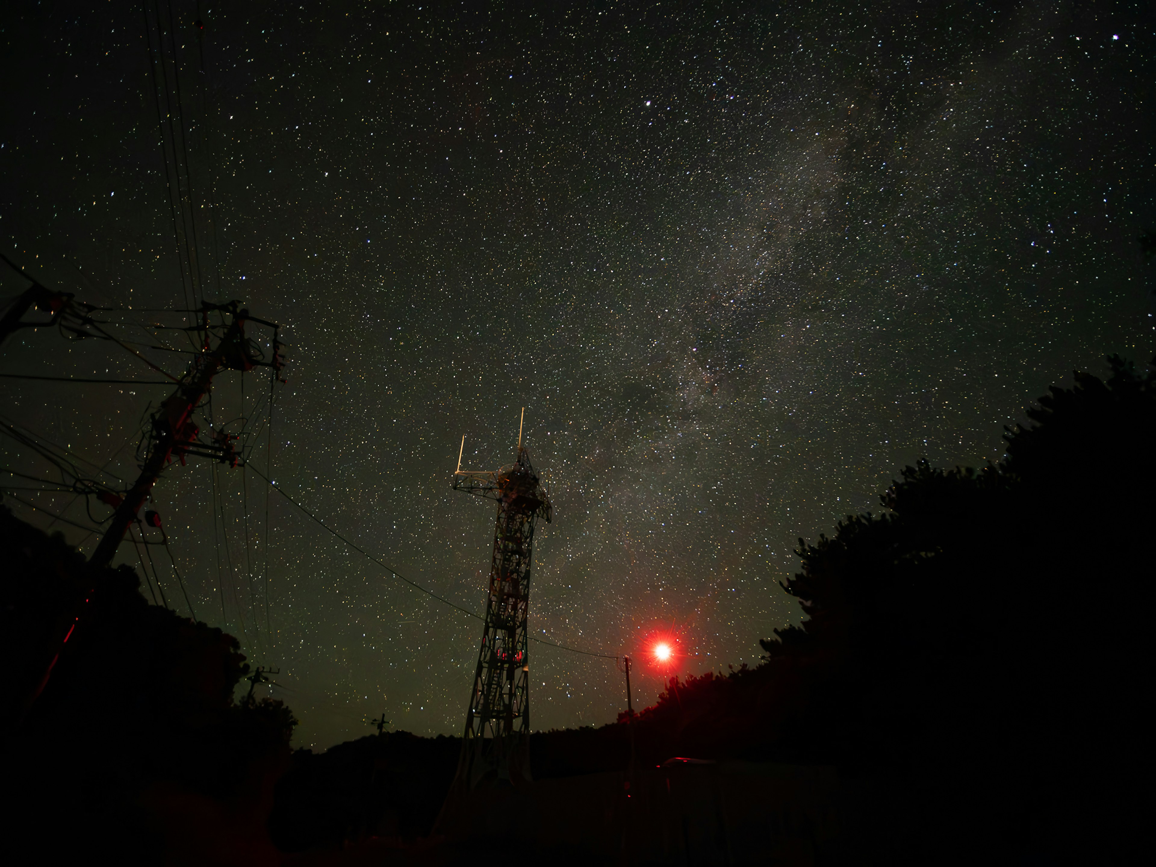 Cielo notturno stellato con una torre di comunicazione e una luce rossa