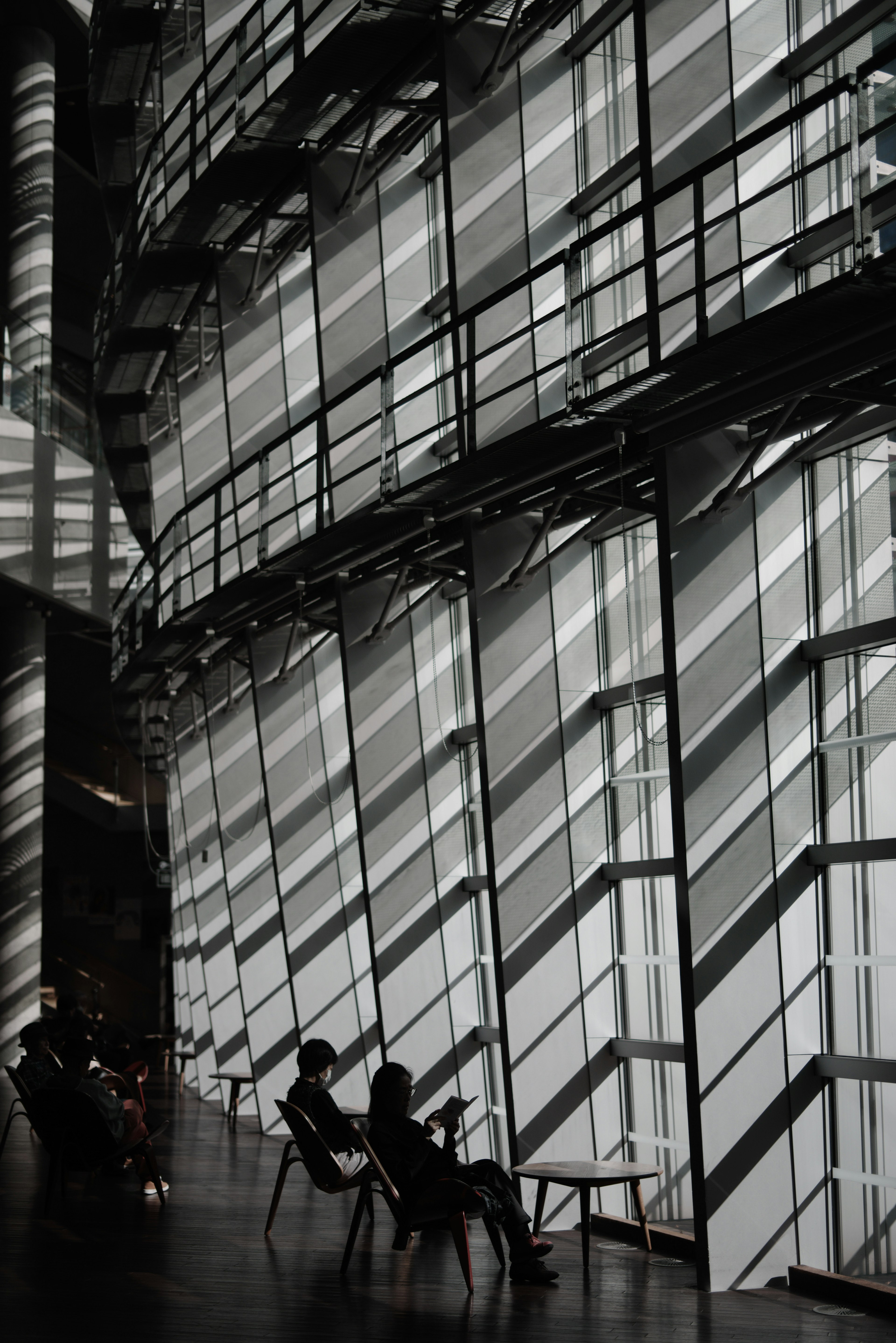 Personas sentadas en un espacio arquitectónico moderno con patrones de luz y sombra que se cruzan en las paredes