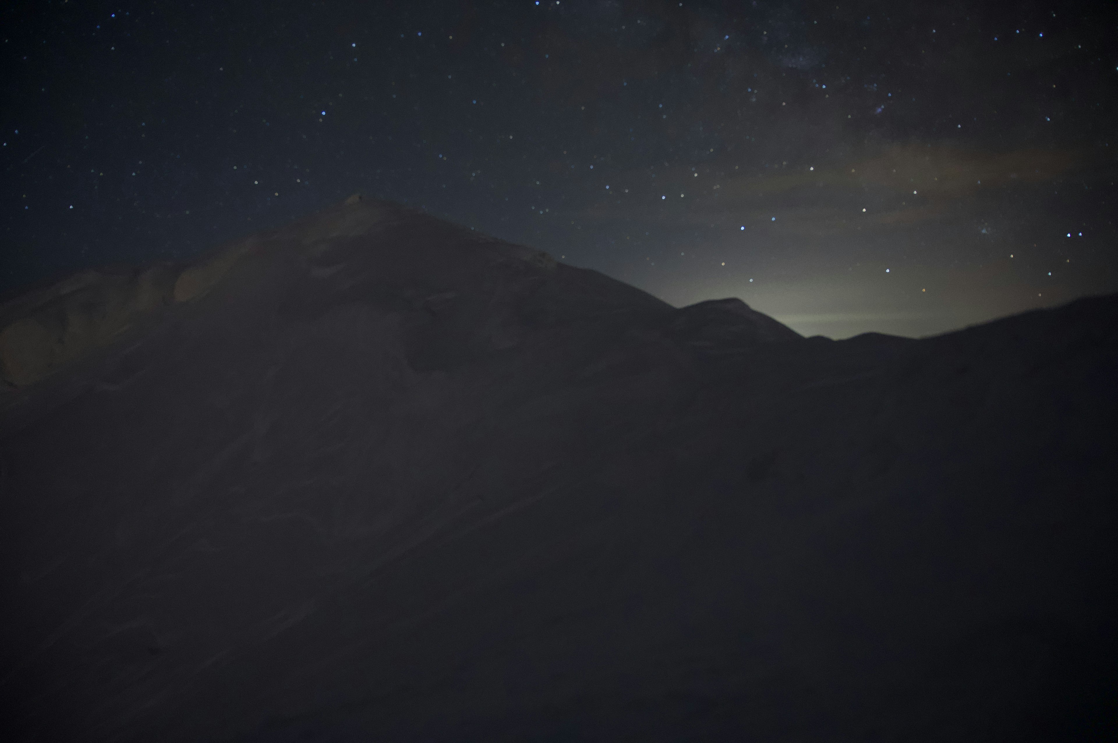 星空の下にある山のシルエットと微かな光