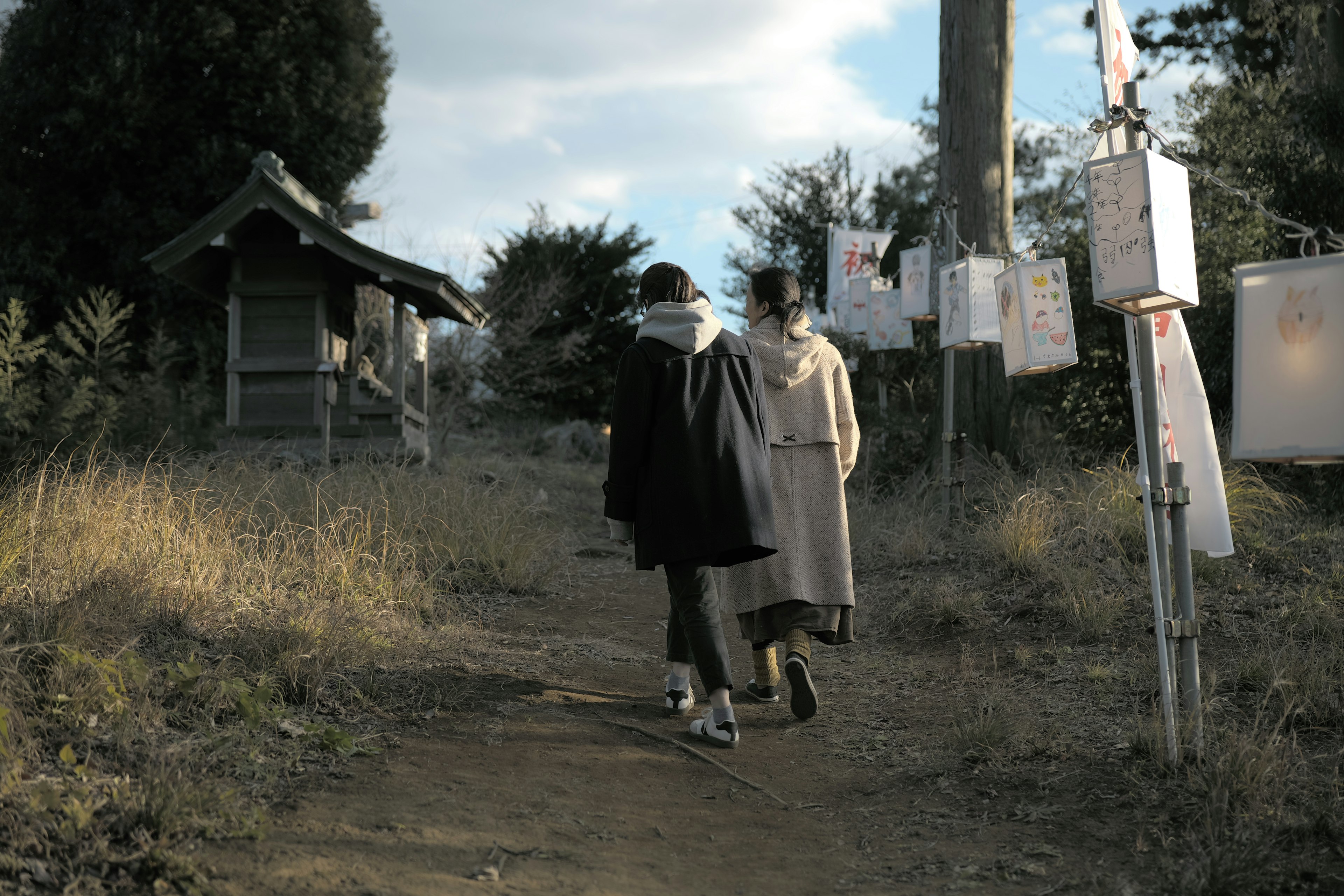 Two figures walking along a path with a shrine-like structure nearby