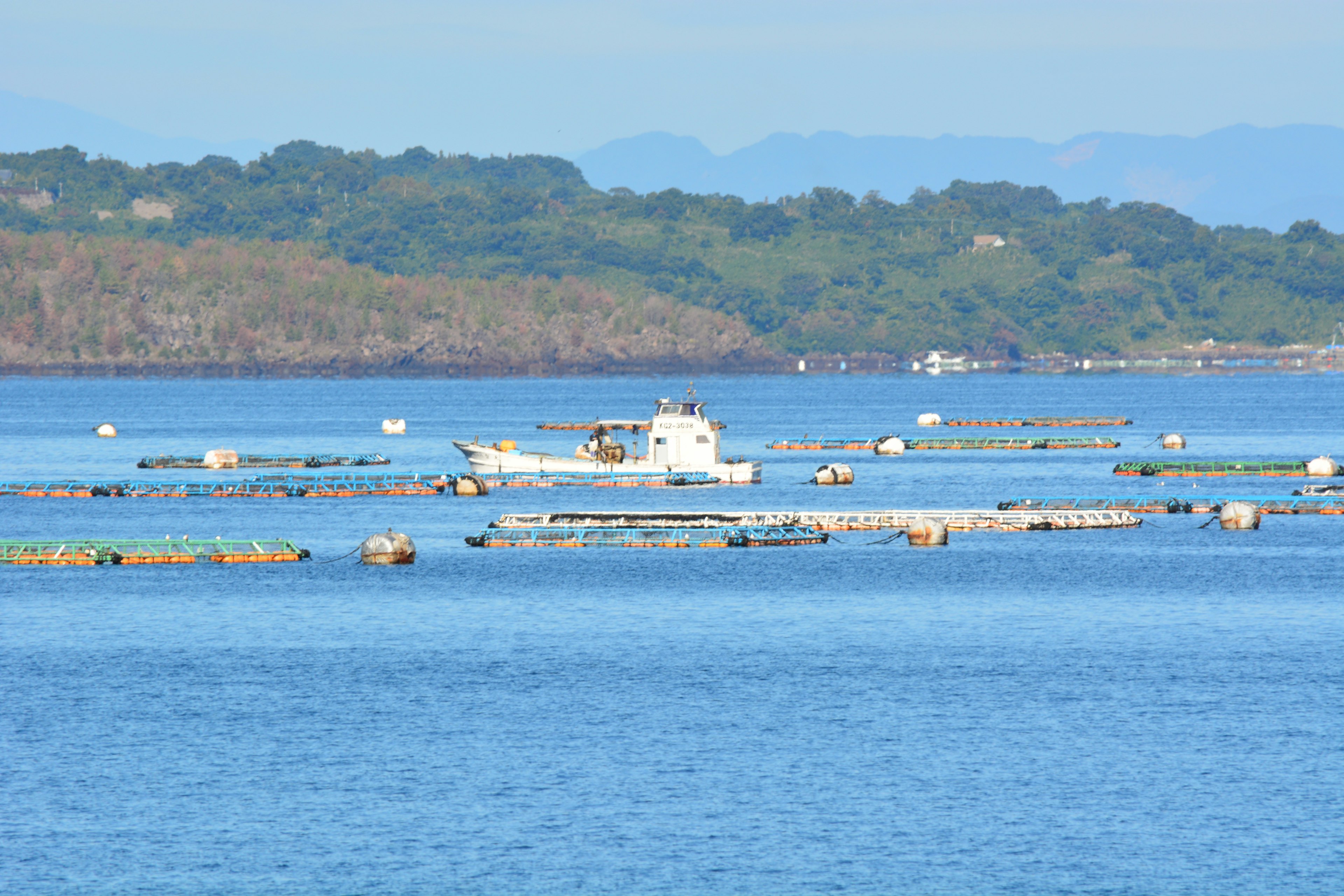 Bateau de pêche sur l'eau bleue avec des radeaux d'aquaculture flottants