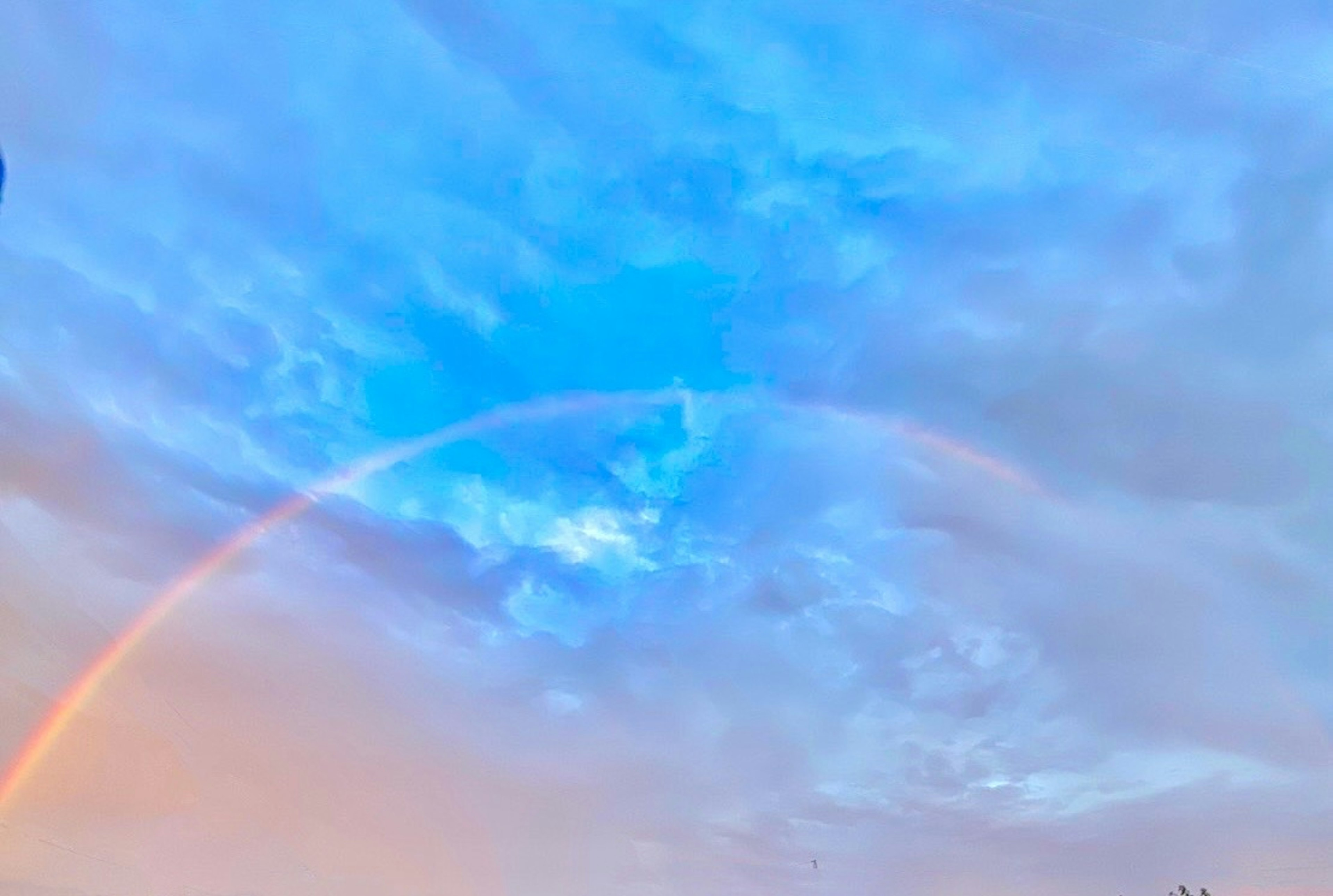 Vista spettacolare di un arcobaleno che si estende attraverso un cielo blu con nuvole