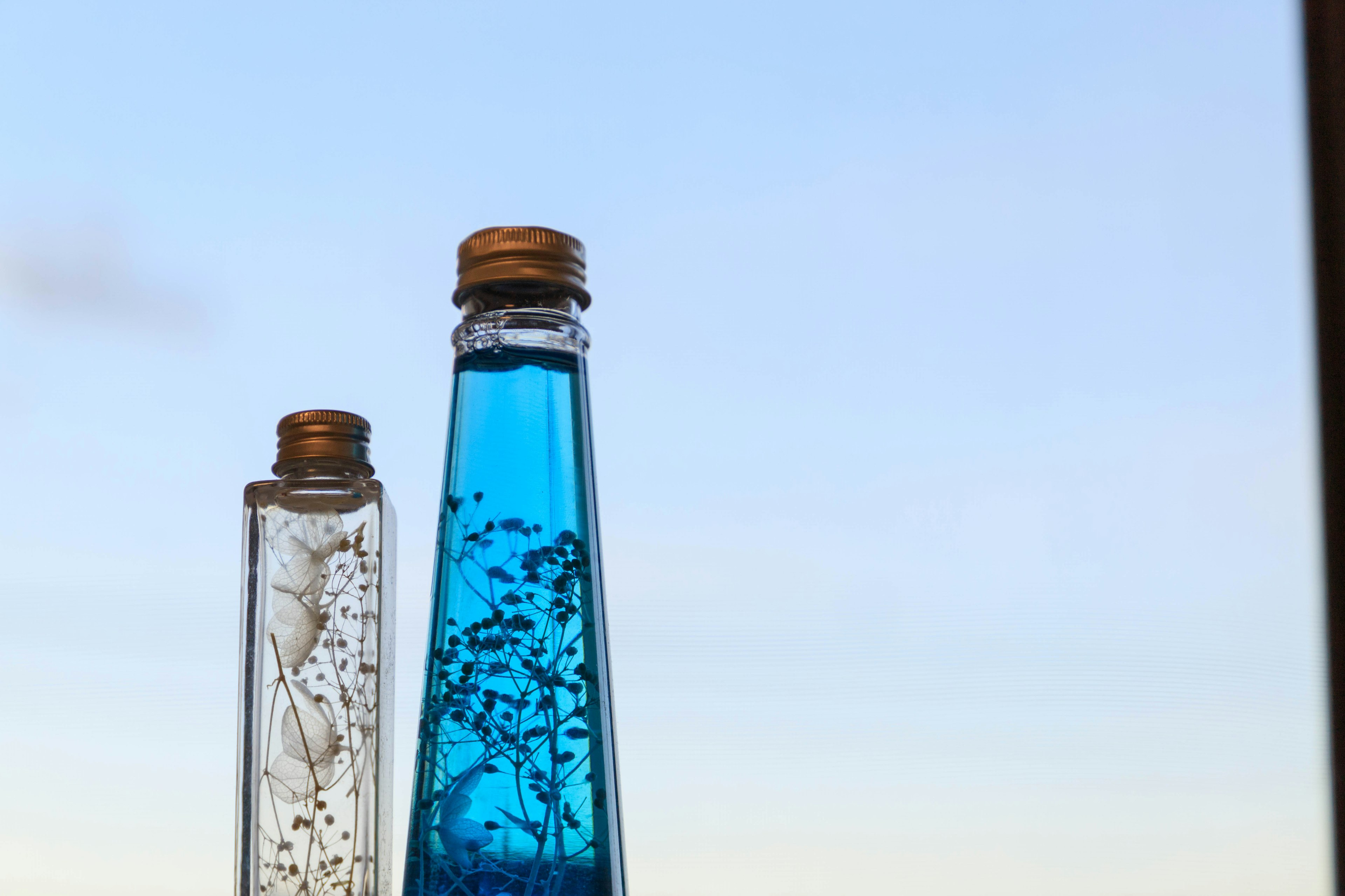 Two decorative bottles one with blue liquid and the other with white flowers against a clear sky