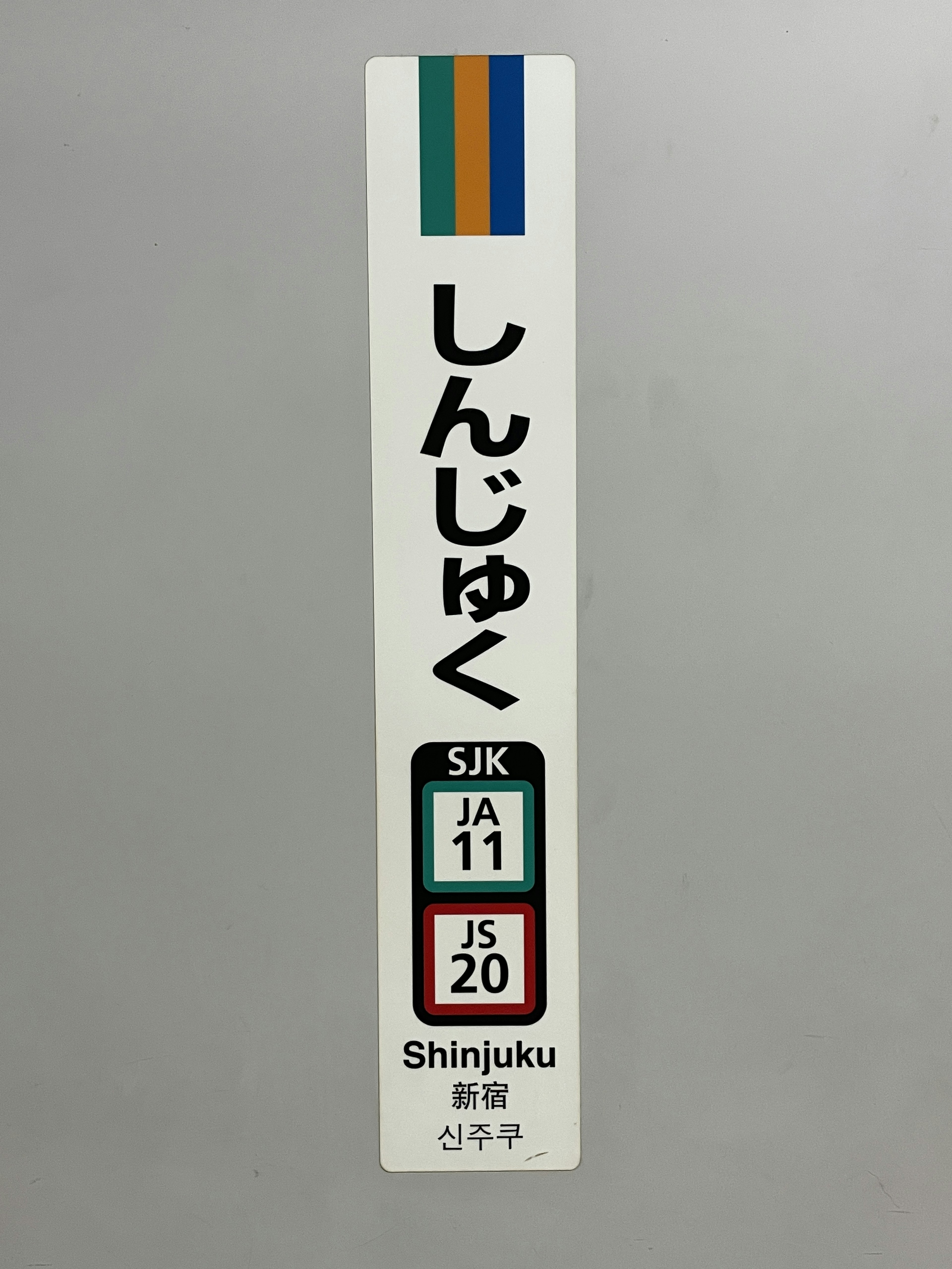 Sign for Shinjuku Station featuring colored bars and Japanese and English text