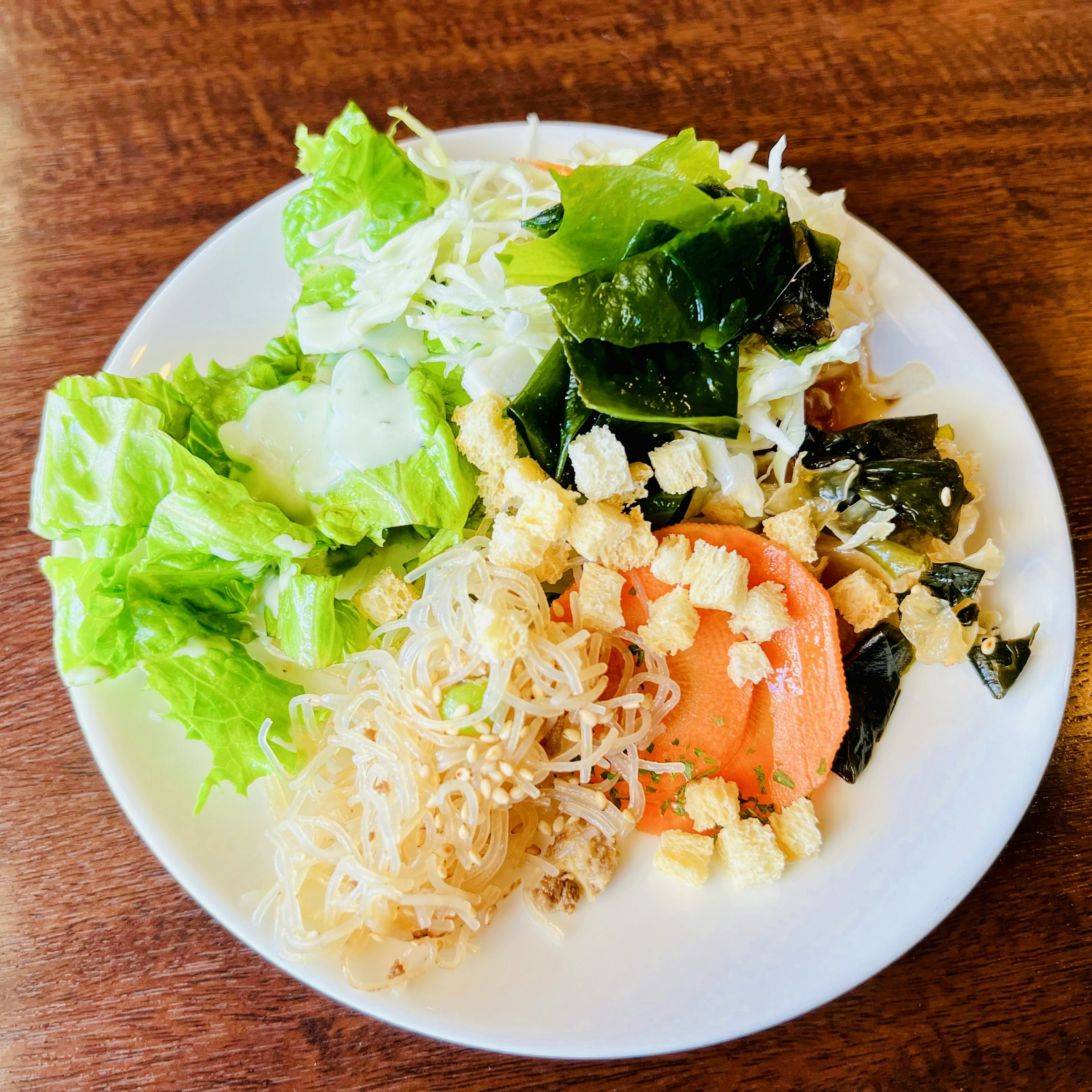 Un plato blanco con una ensalada que incluye verduras de hoja verde y algas