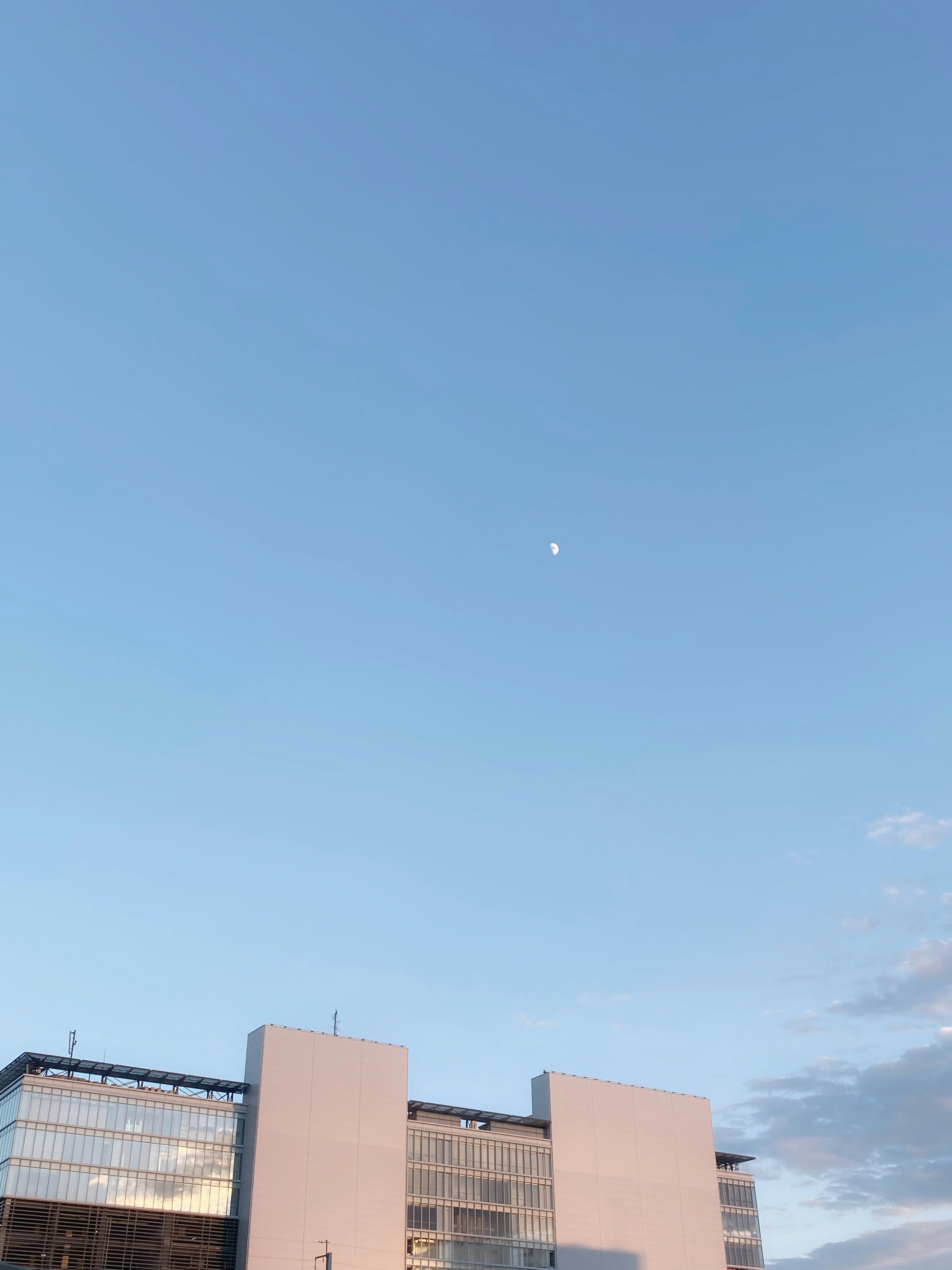 Un bâtiment moderne sous un ciel bleu clair avec une lune visible