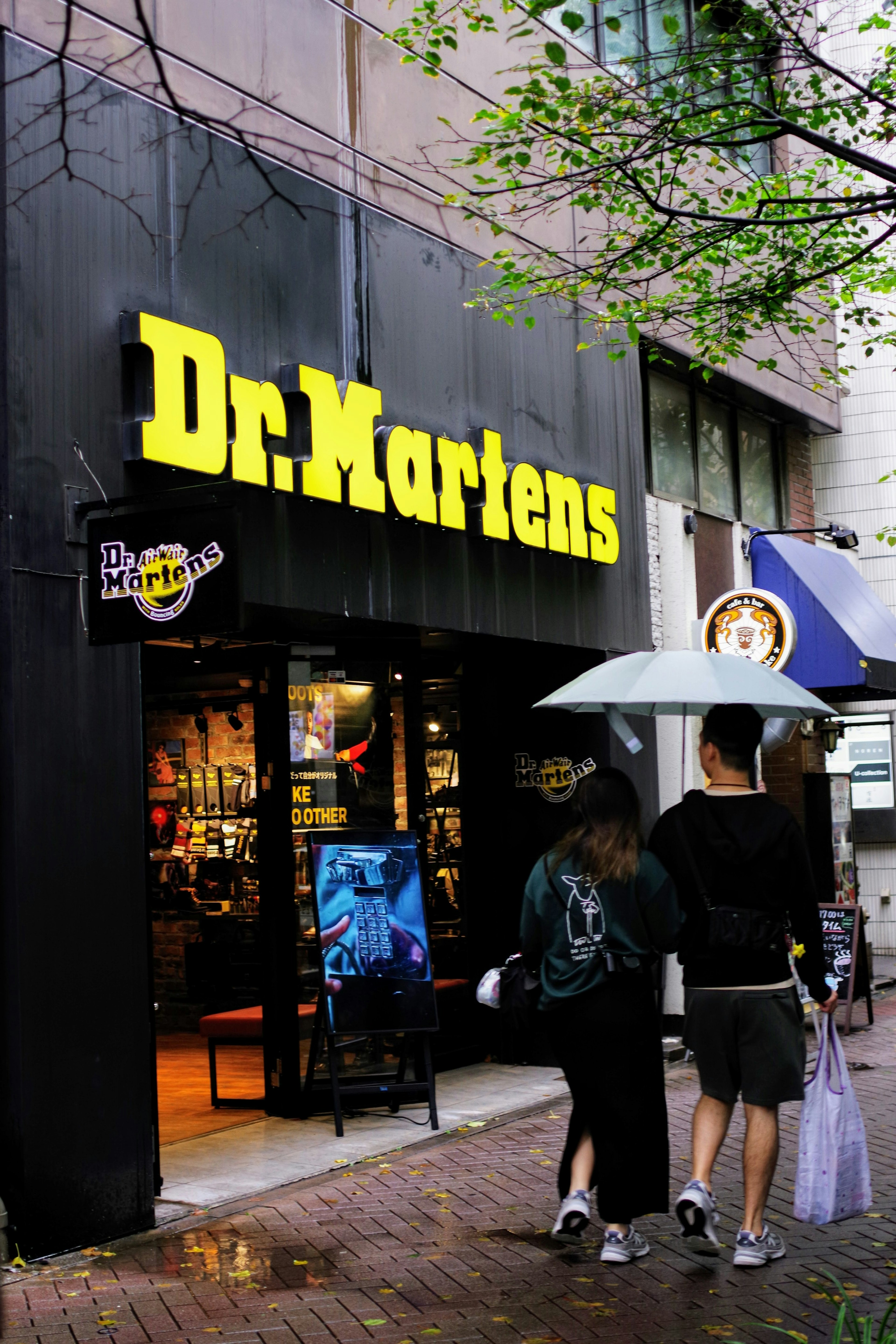 Couple marchant devant un magasin Dr Martens par une journée pluvieuse avec un parapluie