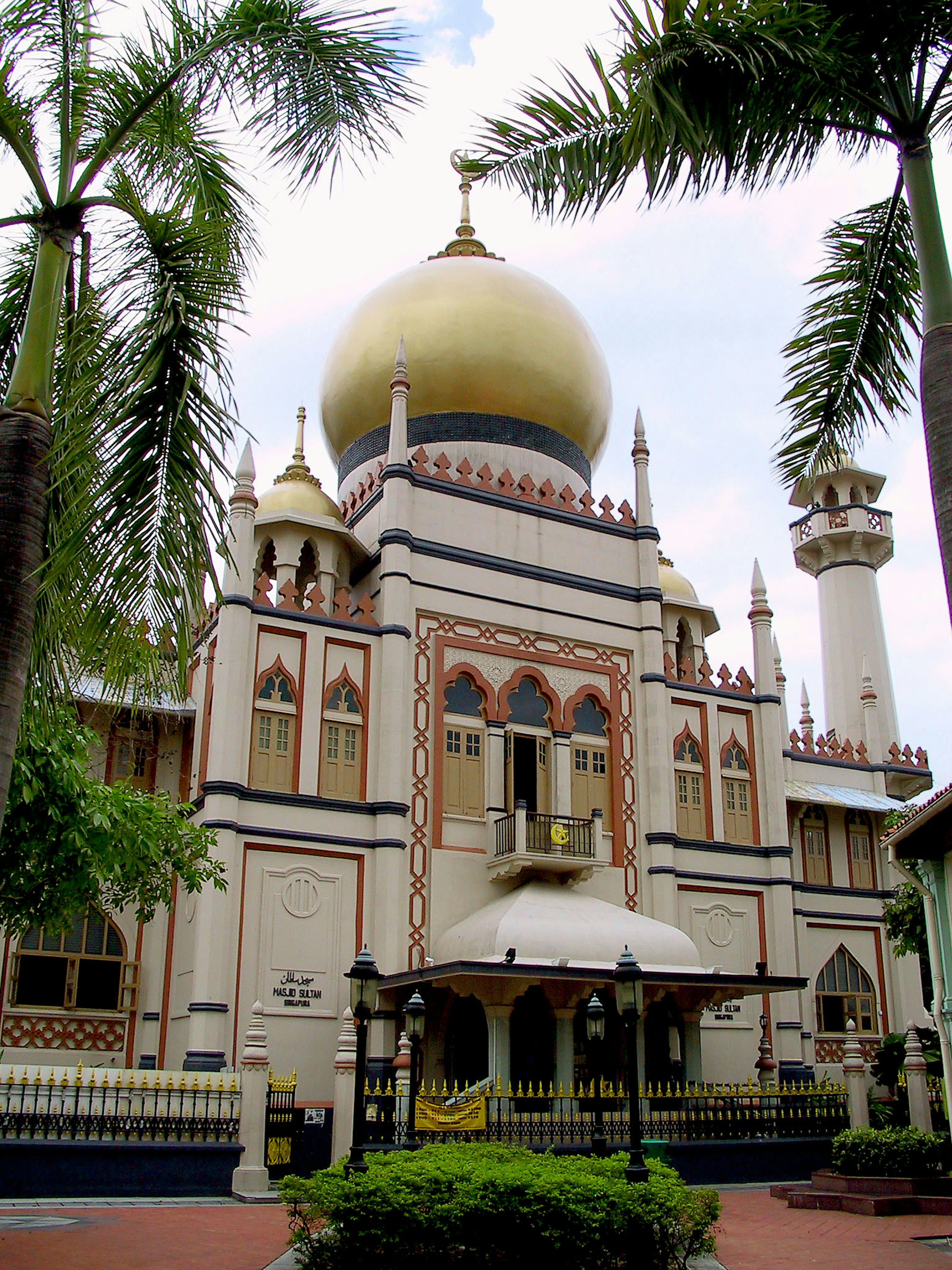 Extérieur d'une mosquée avec un dôme doré et des décorations élaborées entourées de verdure