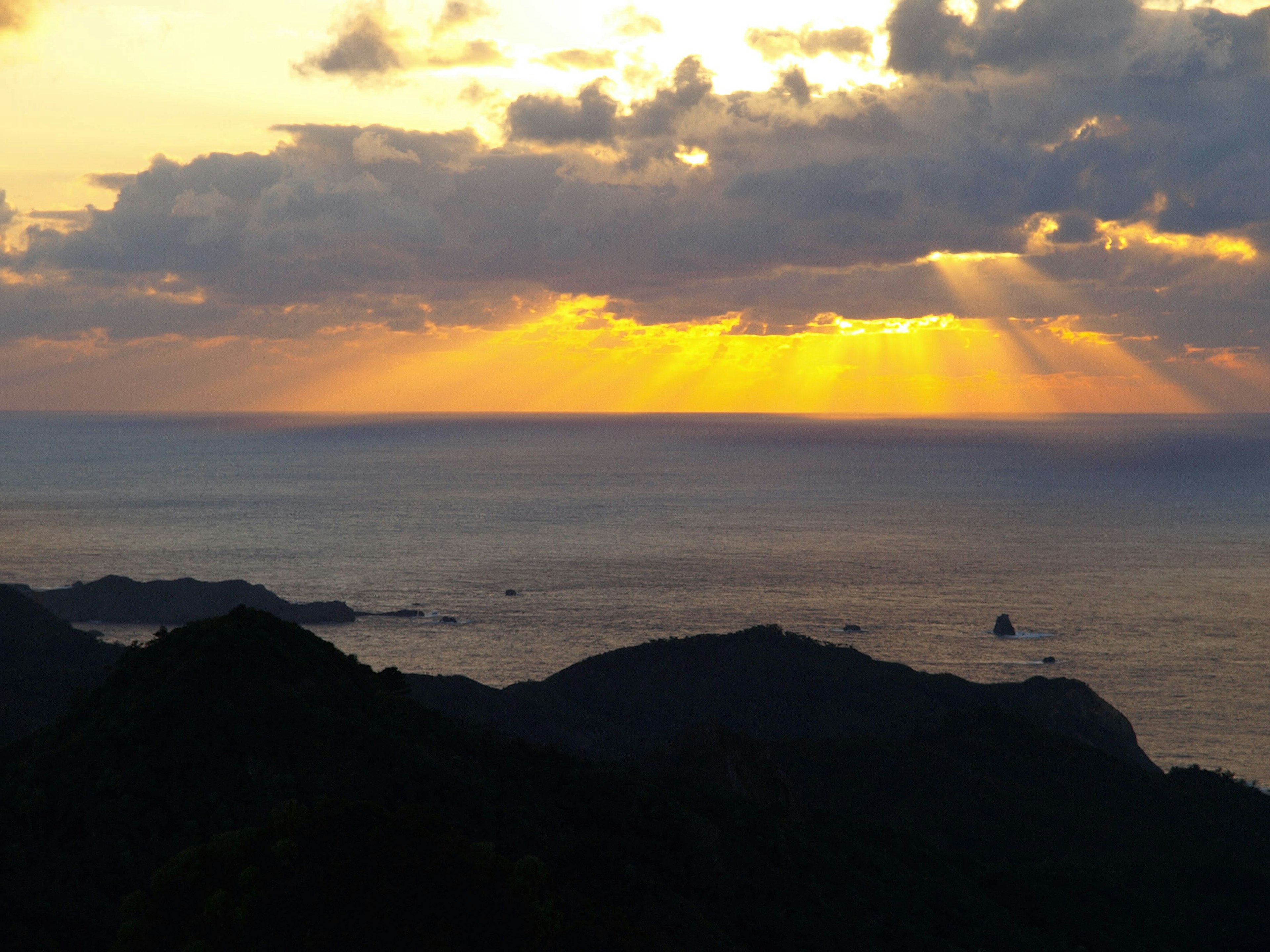 美しい夕日が海に沈む瞬間で、雲の間から光が差し込んでいる