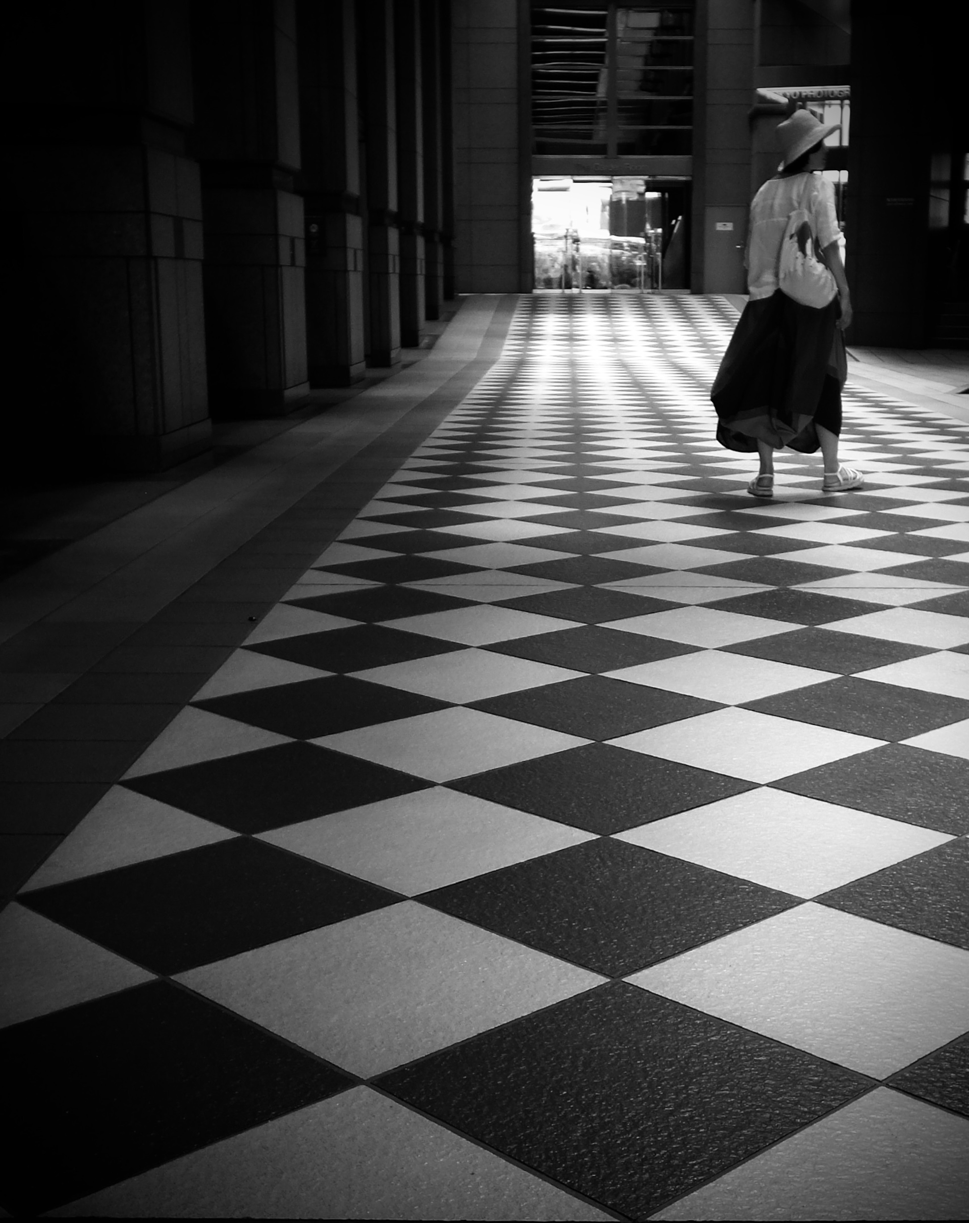 Silueta de una persona caminando sobre un suelo de ajedrez en blanco y negro