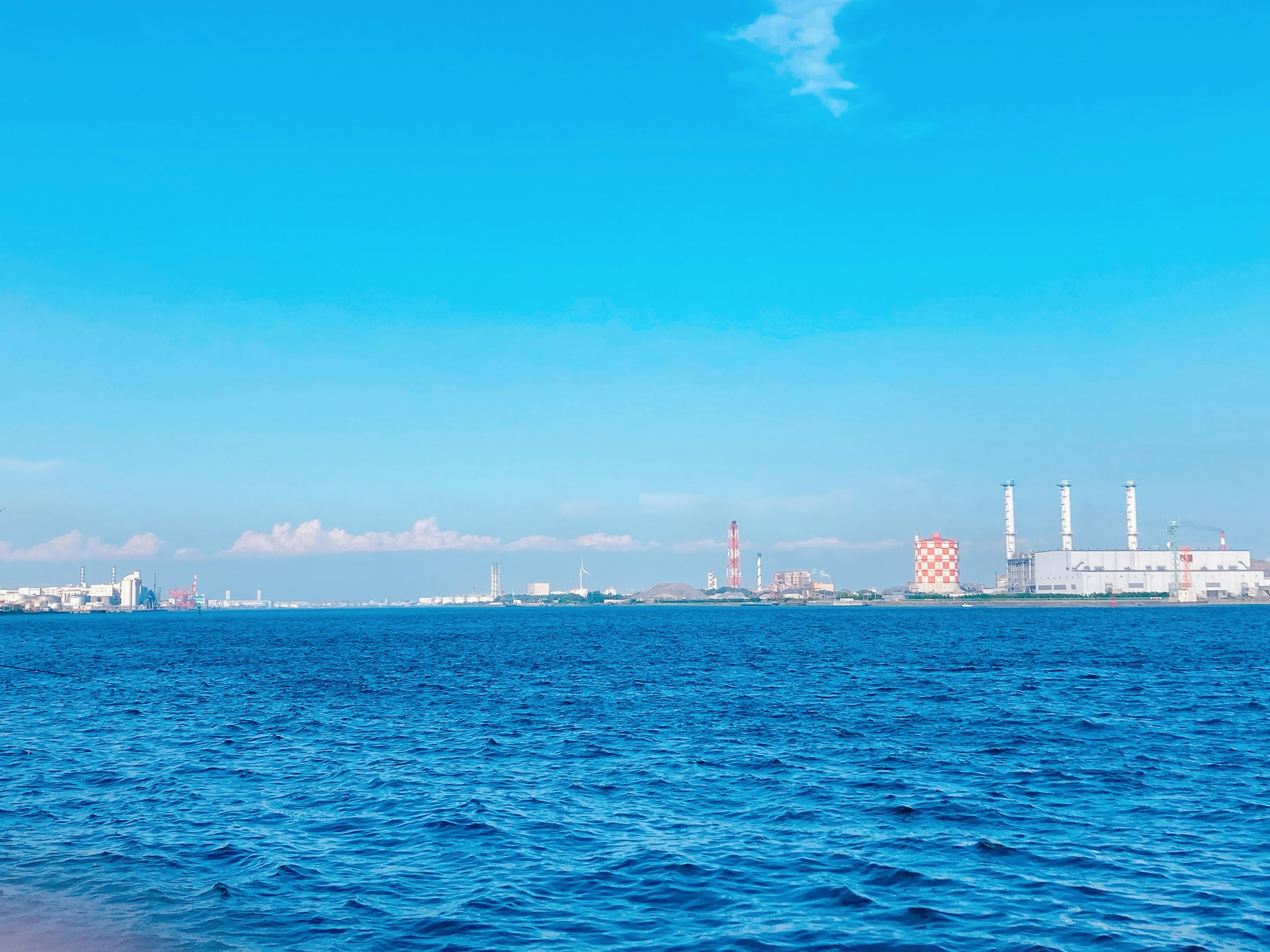 Laut biru cerah dengan bangunan industri dan cerobong asap