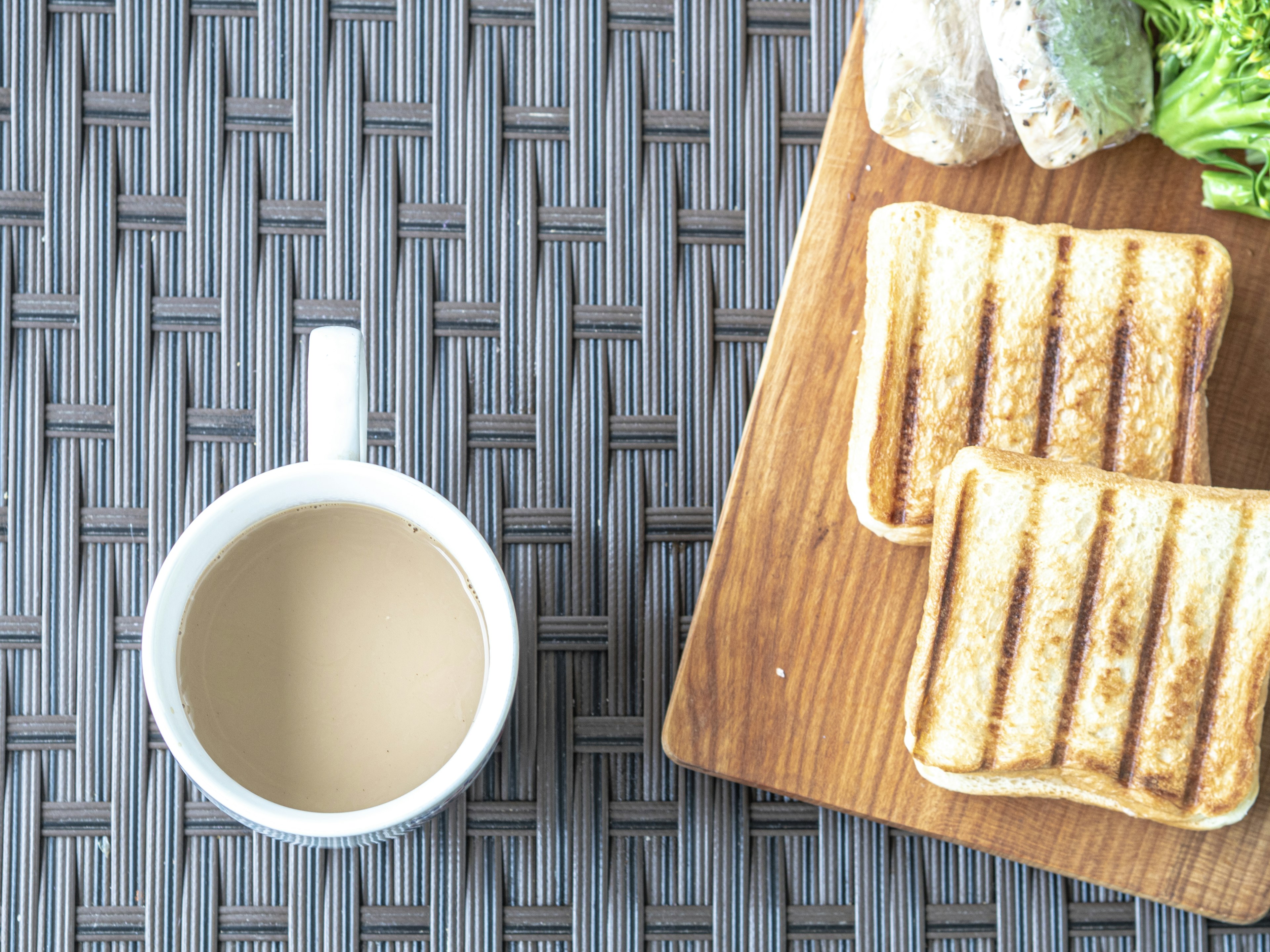 Eine Tasse Kaffee neben geröstetem Brot und Gemüse auf einem Holzbrett