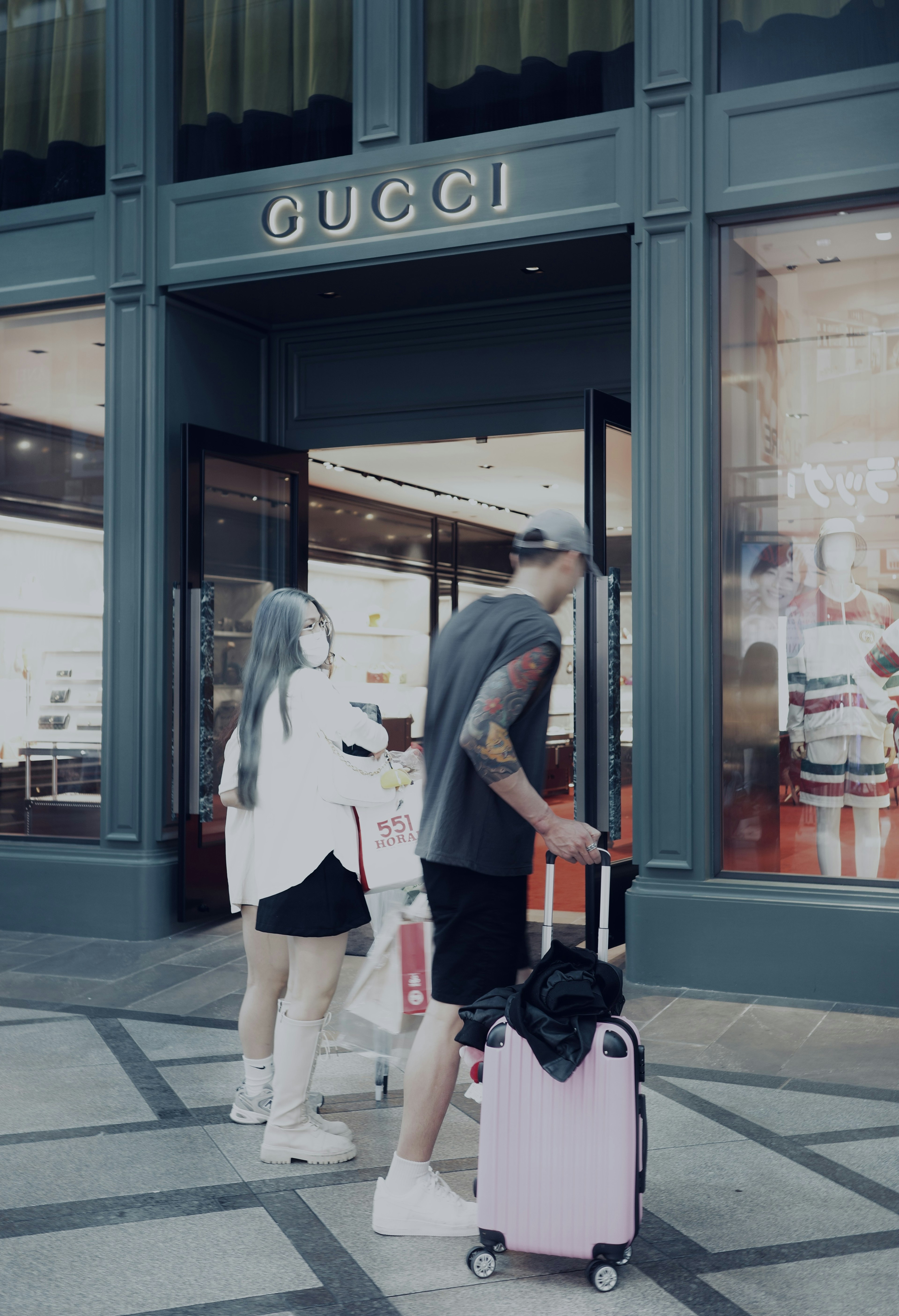 Couple standing in front of Gucci store with luggage