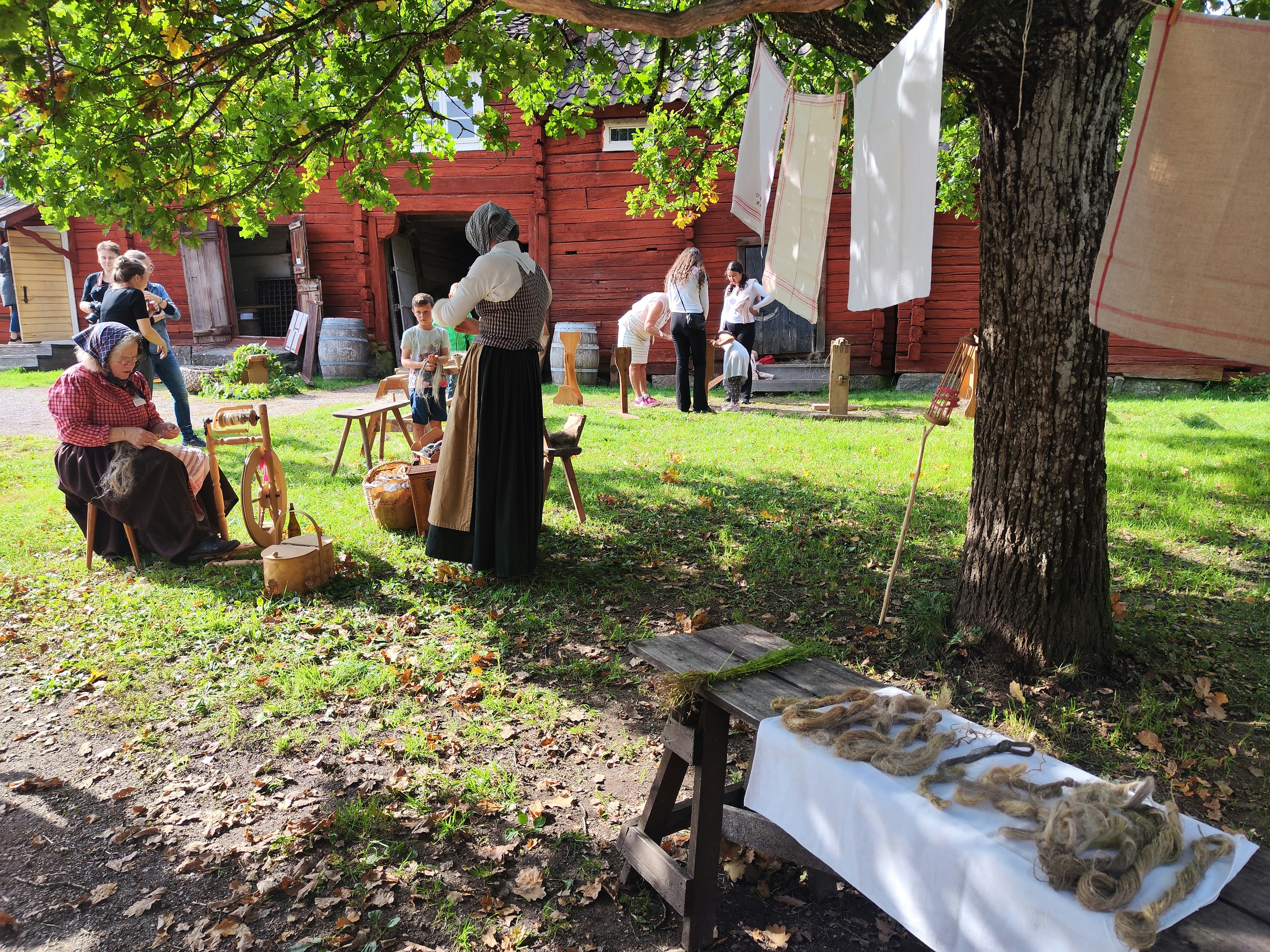 People in traditional clothing engaged in outdoor activities with a red barn in the background