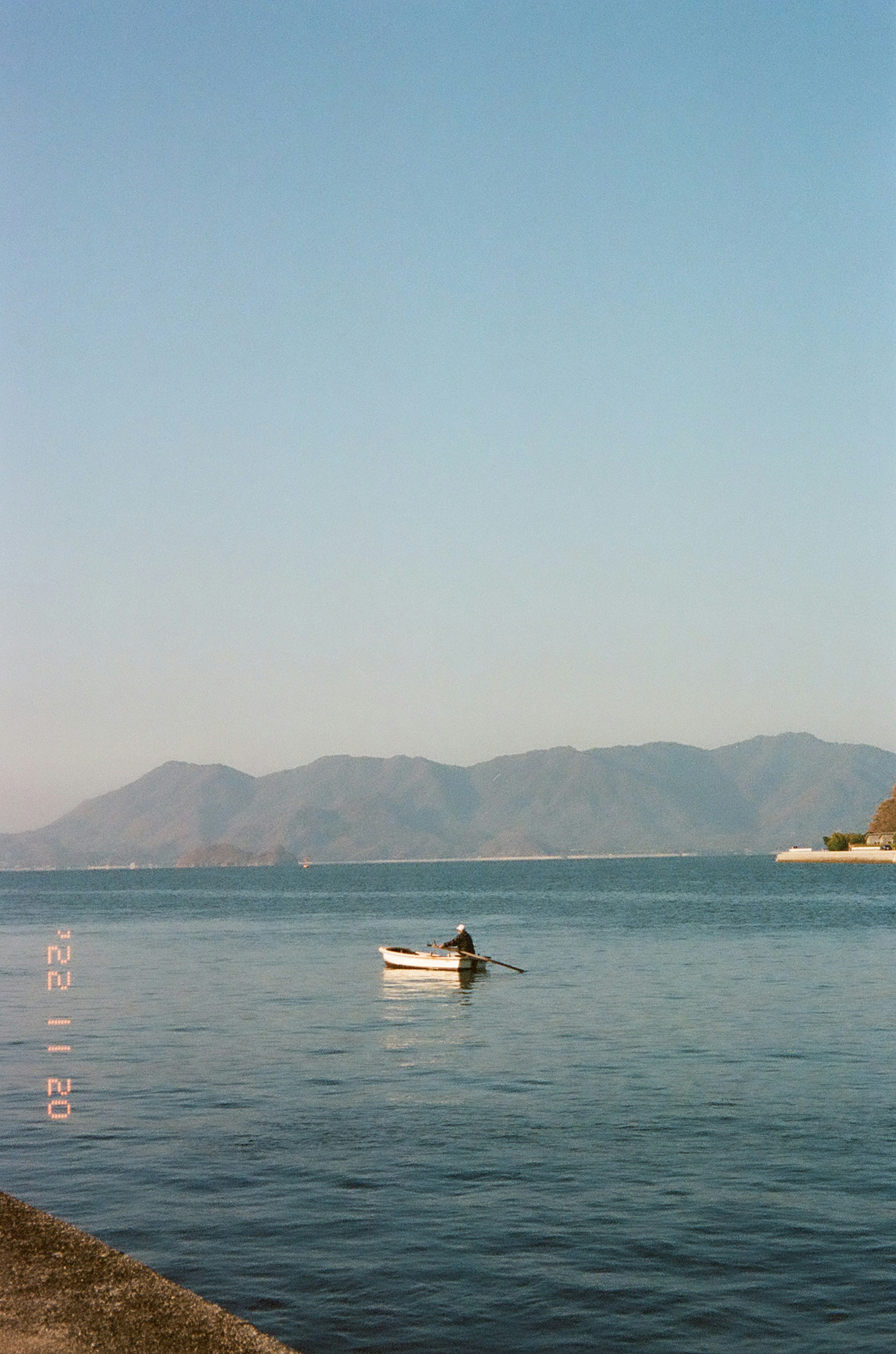 静かな湖に小舟が浮かび、遠くに山々が見える風景