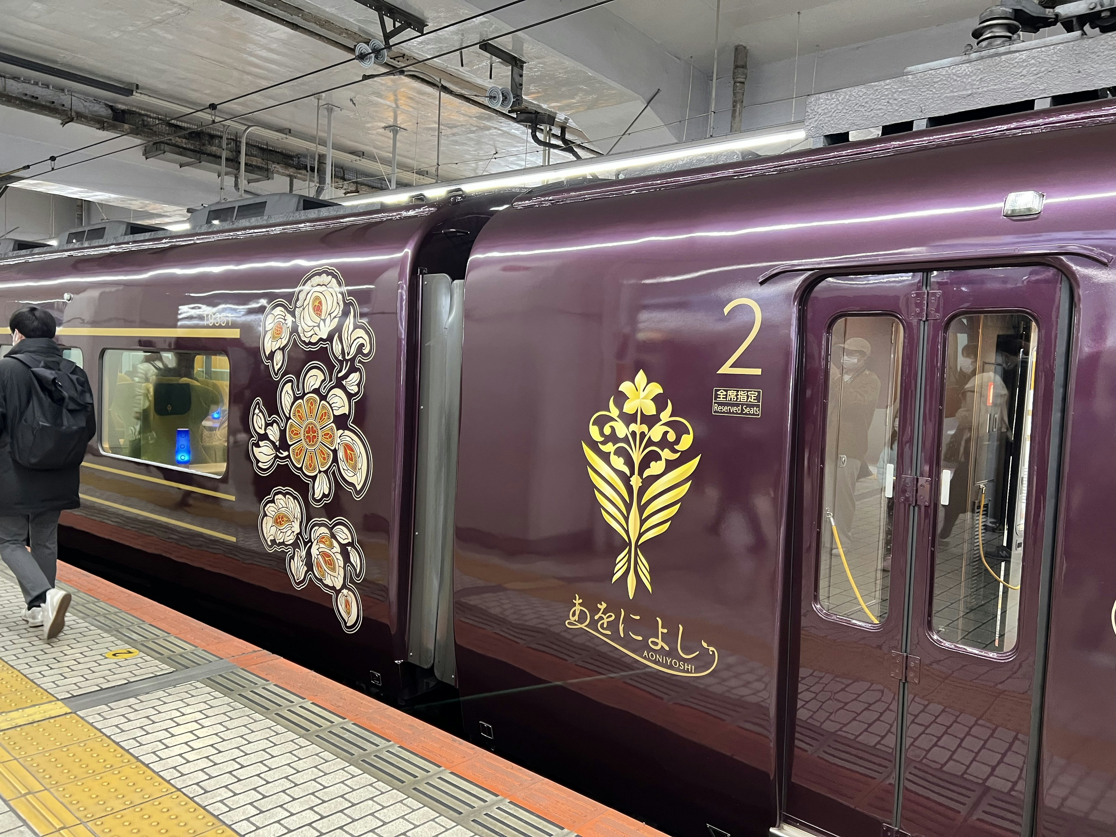 紫色の列車には金色の装飾と花の模様があり、駅のプラットフォームに停車中