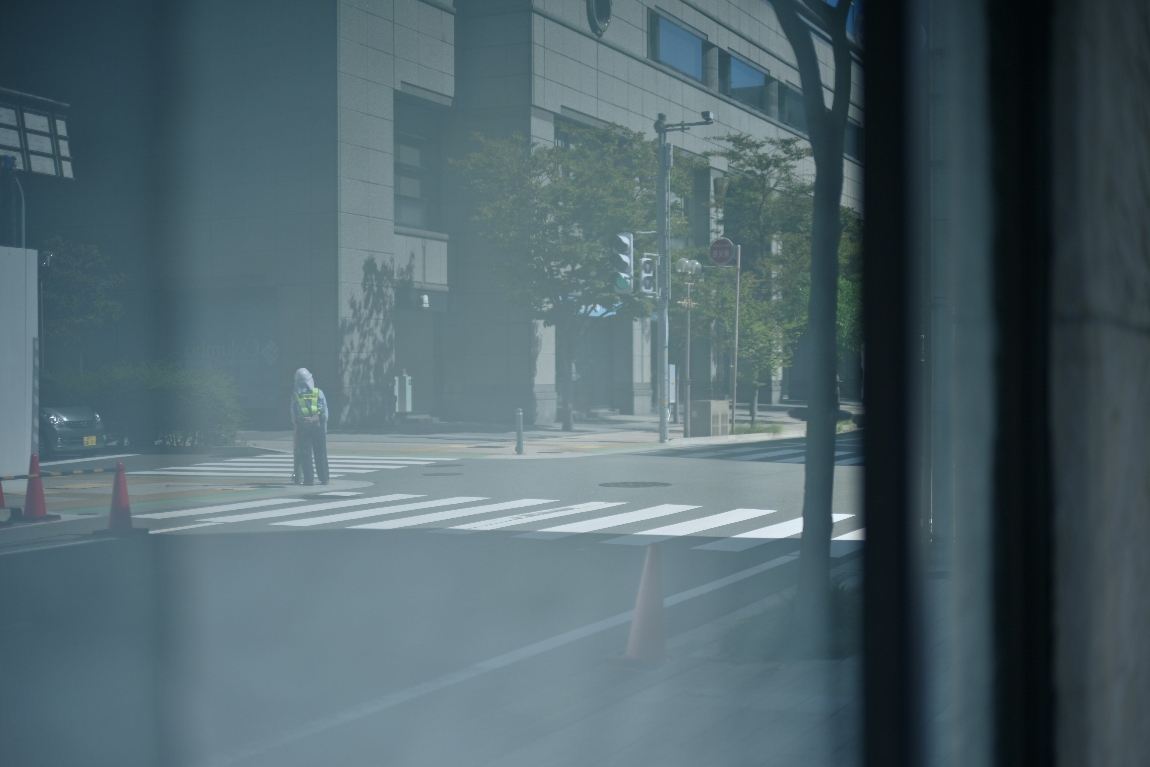 A photo showing a person waiting at a crosswalk with buildings in the background