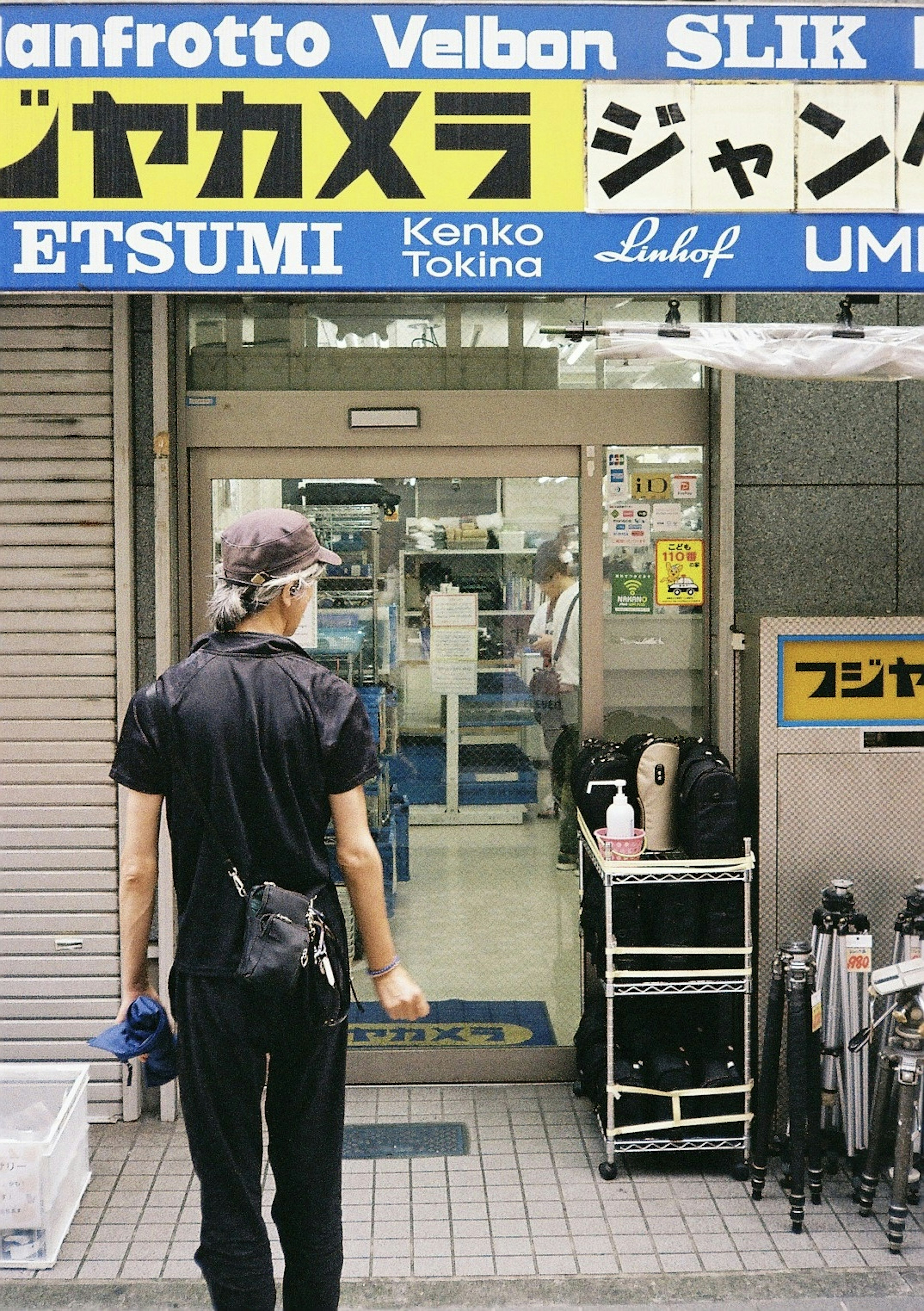 A man in black clothing stands in front of a camera equipment store