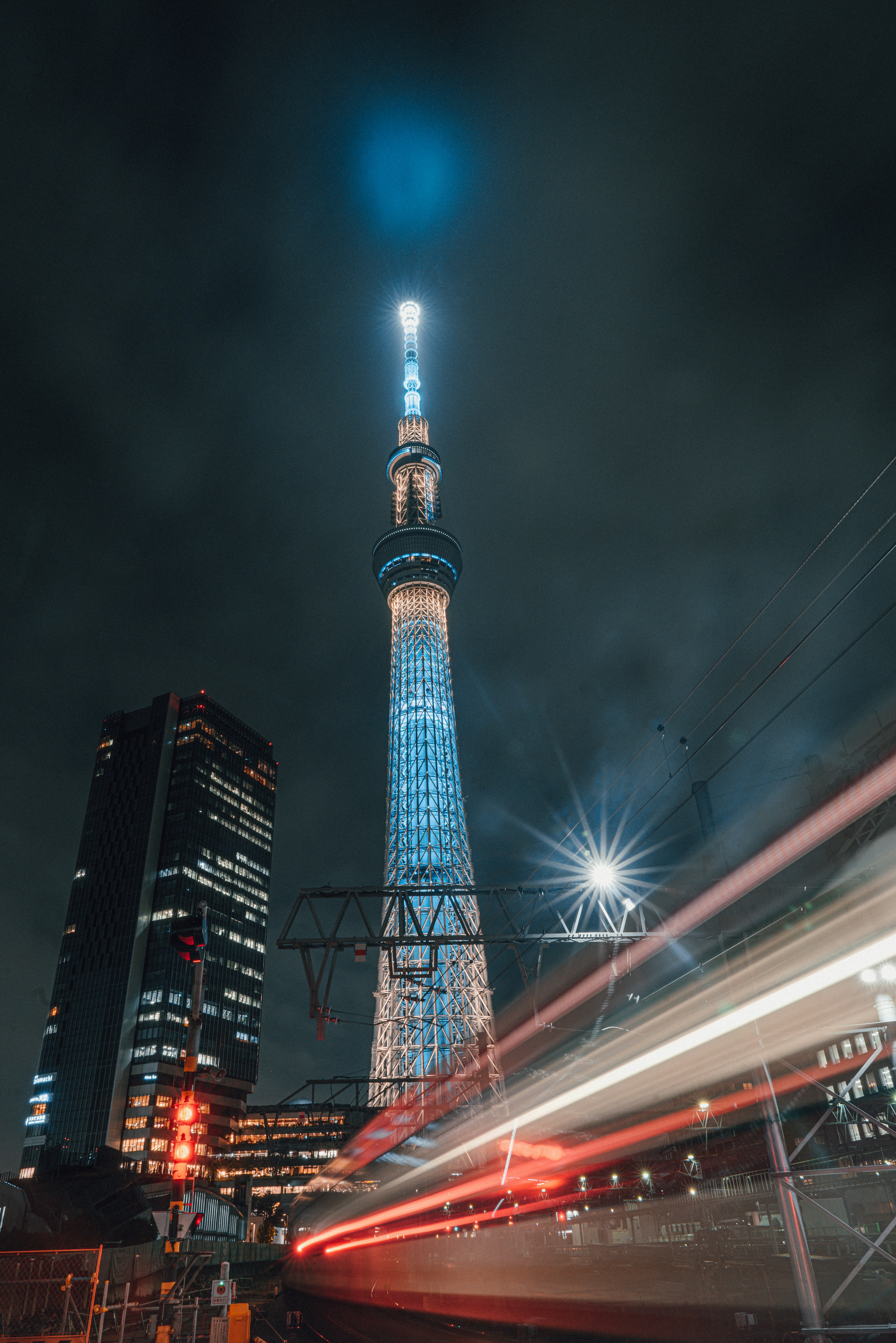 Tokyo Skytree yang diterangi di malam hari dengan bangunan di sekitarnya dan lampu kereta