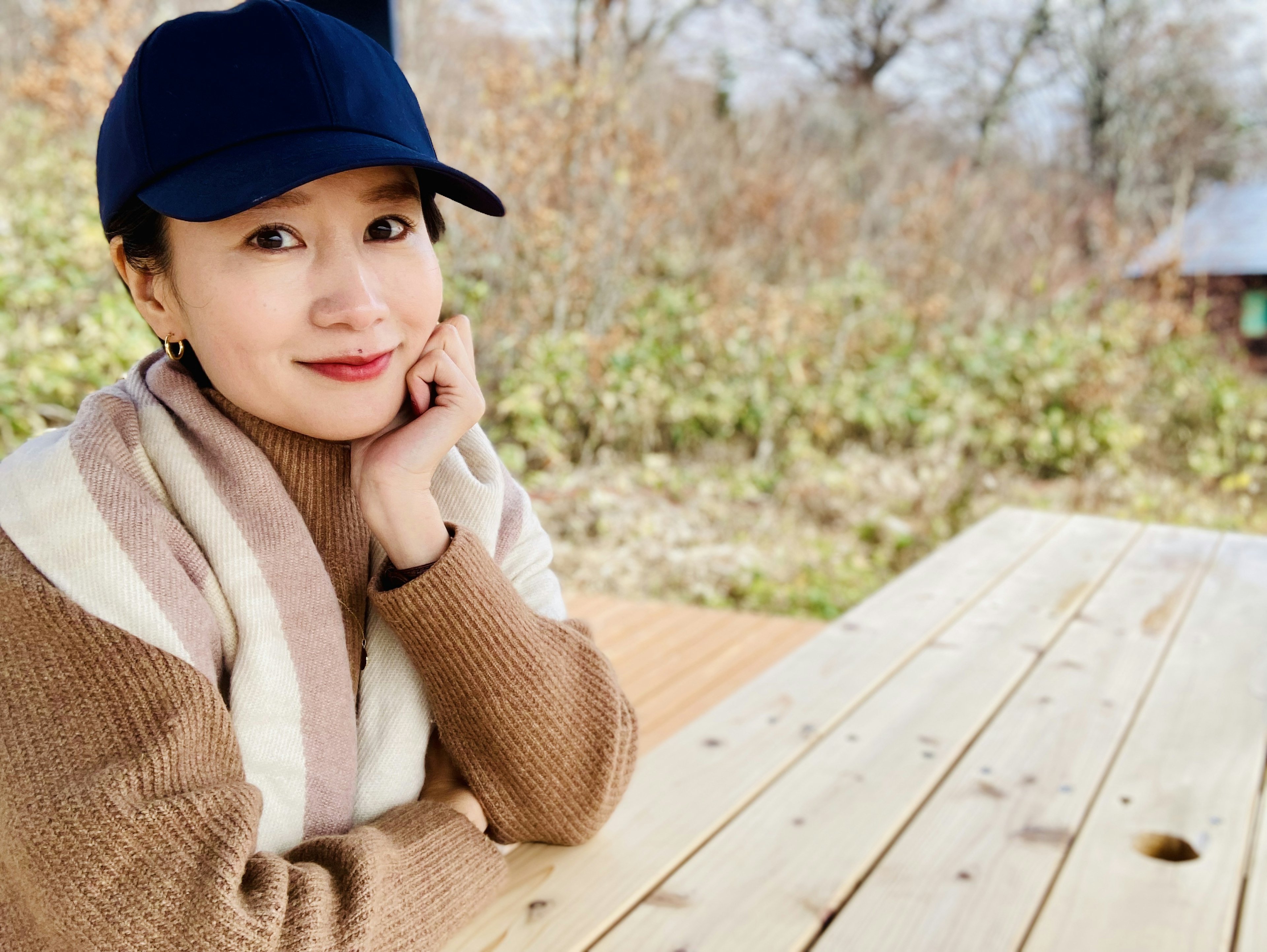 Portrait d'une femme souriante à une table en bois entourée de nature