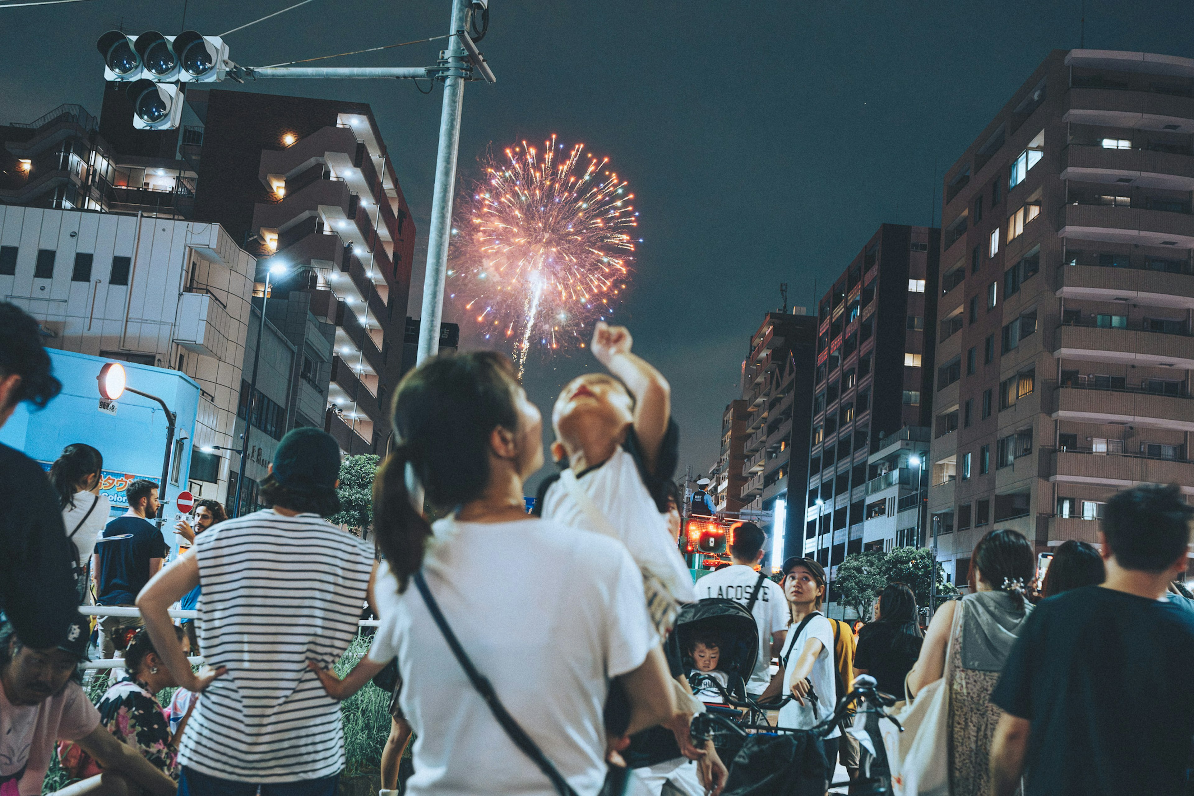 繁忙的街景中，夜空中绽放着烟花，父母抱着孩子