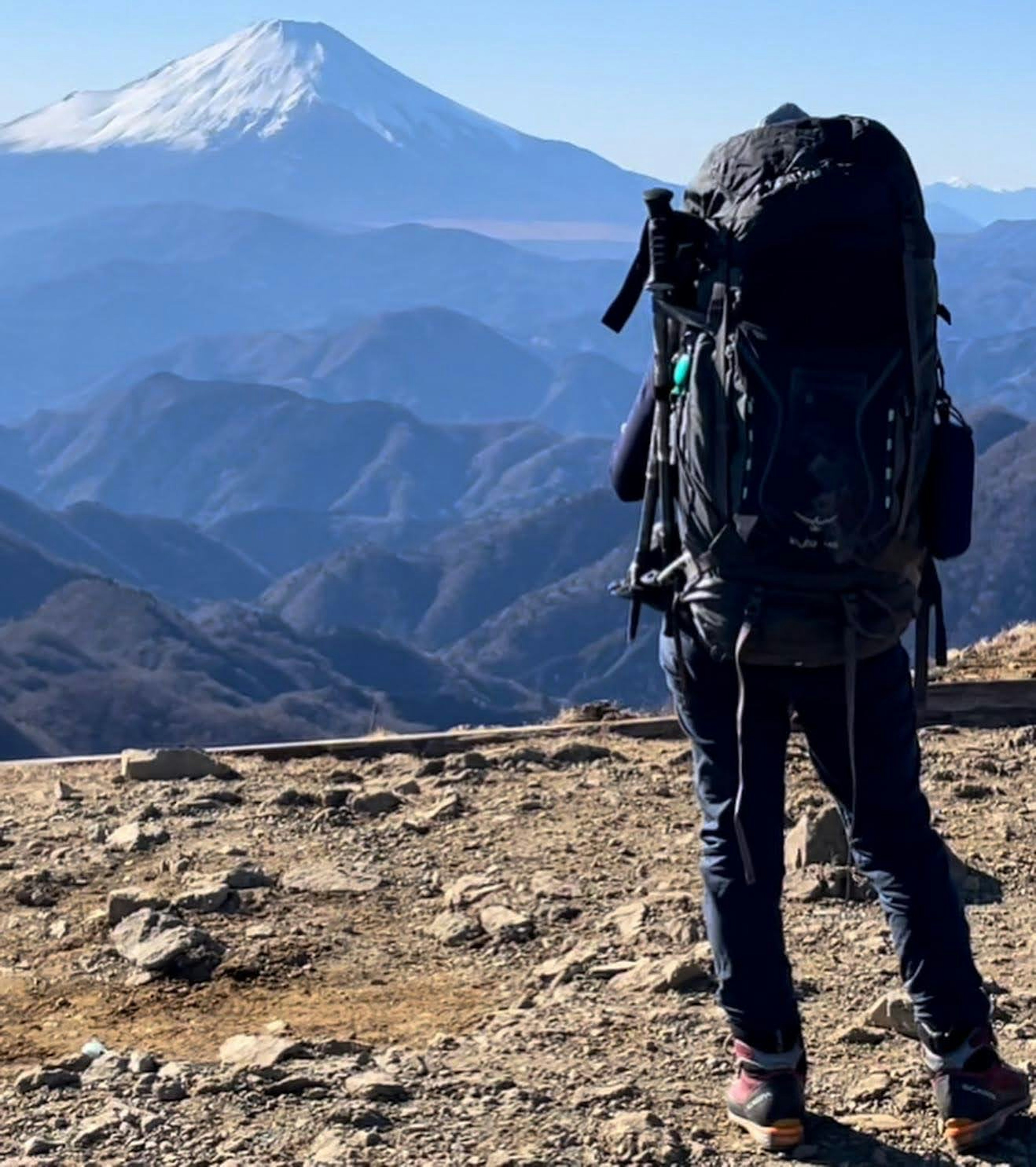 登山者が大きなバックパックを背負い、遠くに雪をかぶった山を眺めている