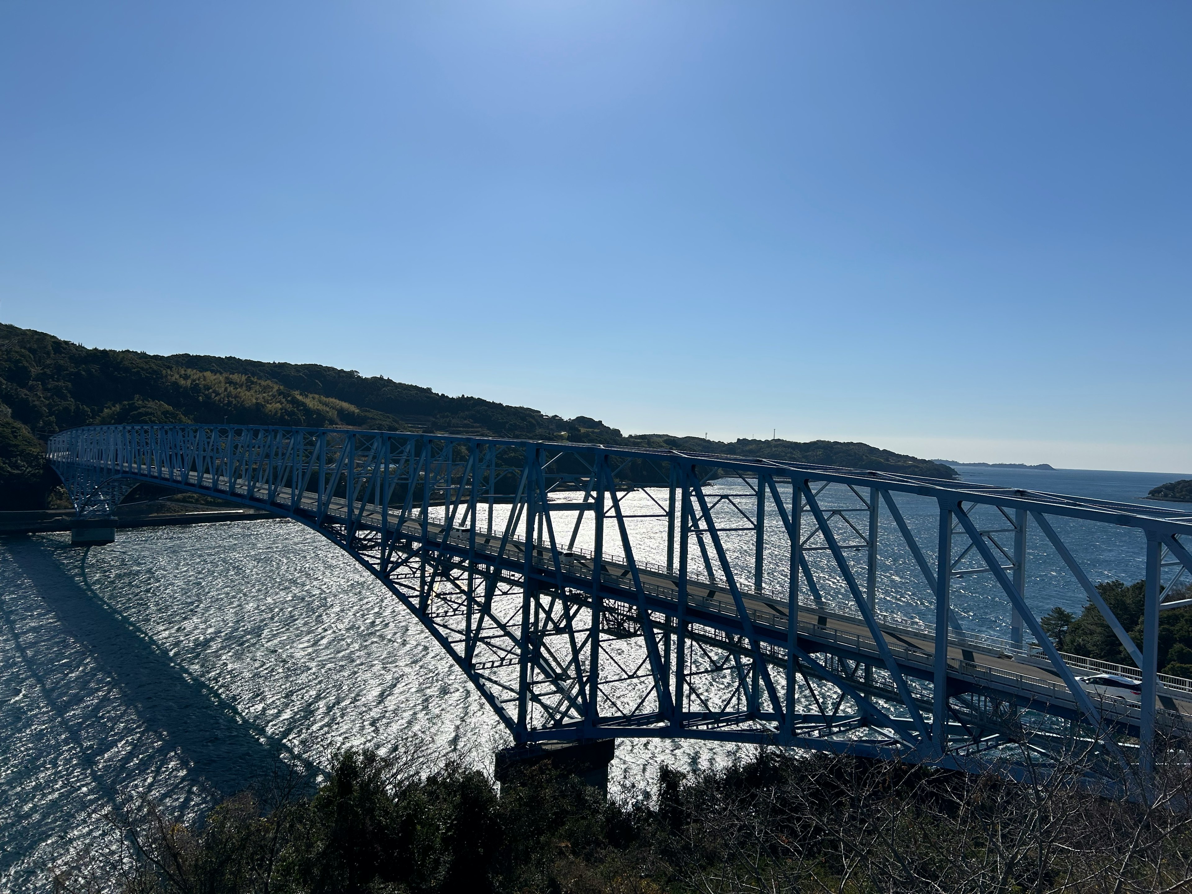 A blue bridge spanning across a shimmering sea under a clear blue sky