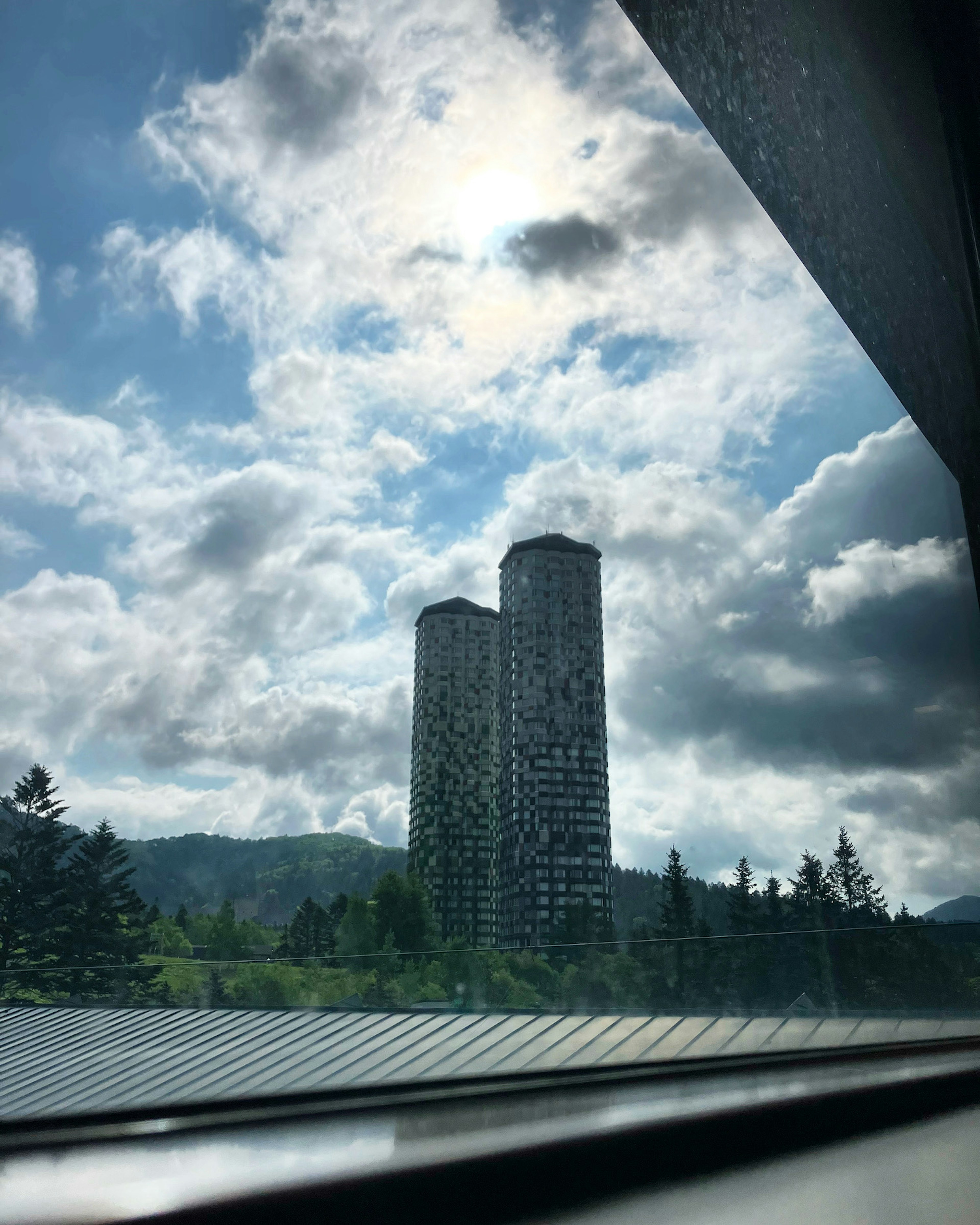 Two tall buildings visible through a window with blue sky and clouds