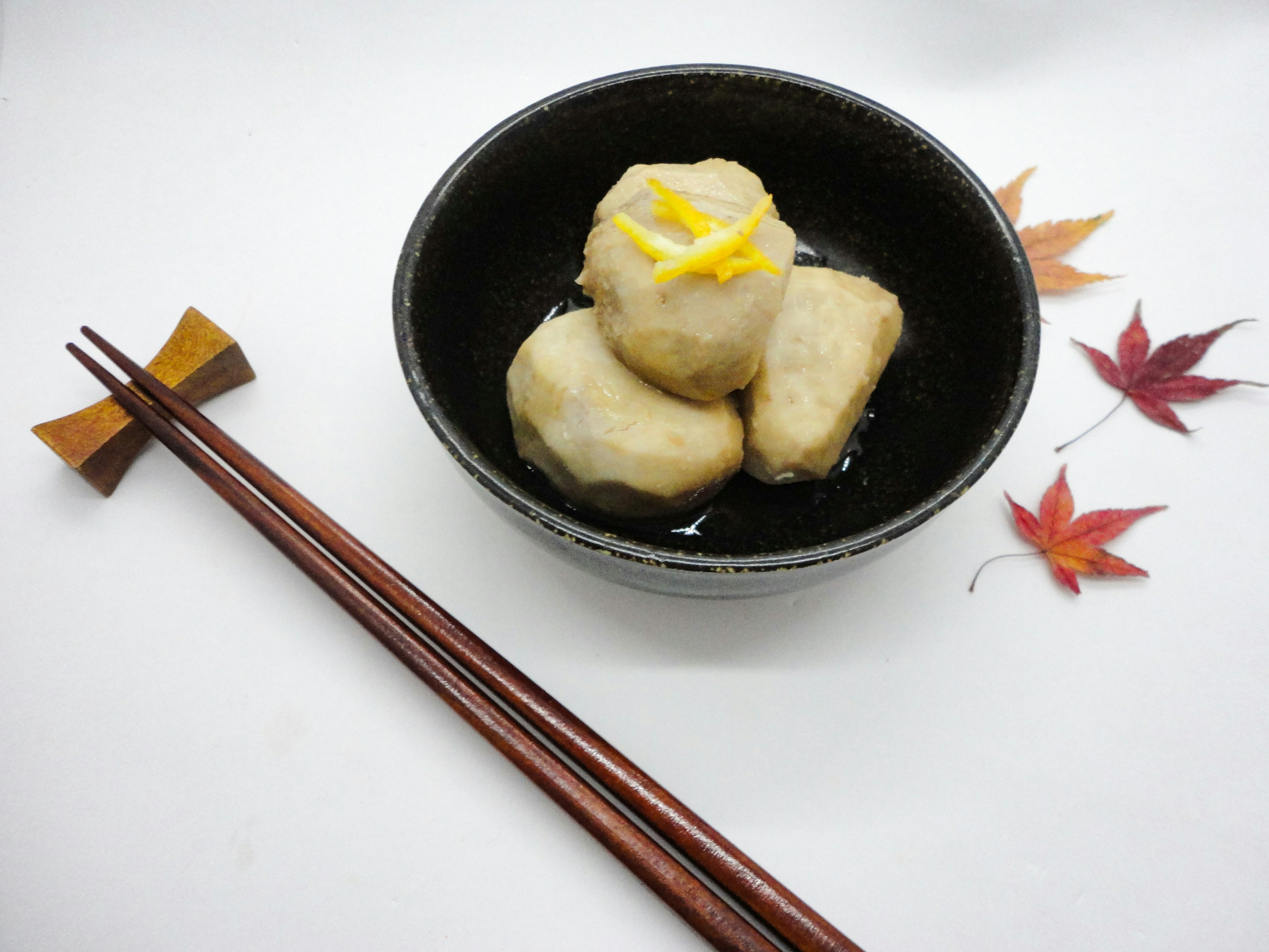 Trois boulettes blanches dans un bol noir surmontées de zeste jaune entourées de feuilles d'automne