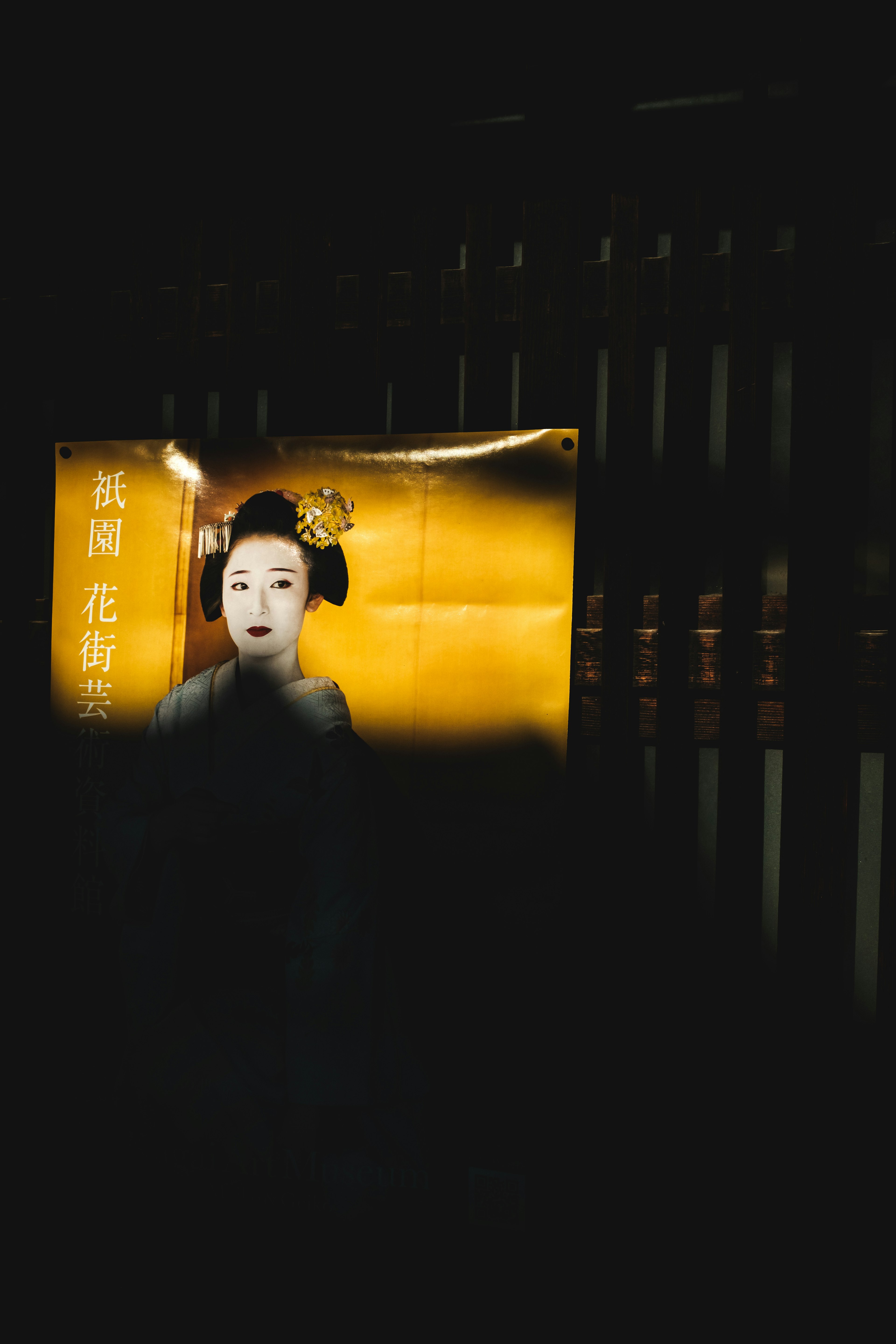 A poster of a Japanese maiko illuminated against a dark background