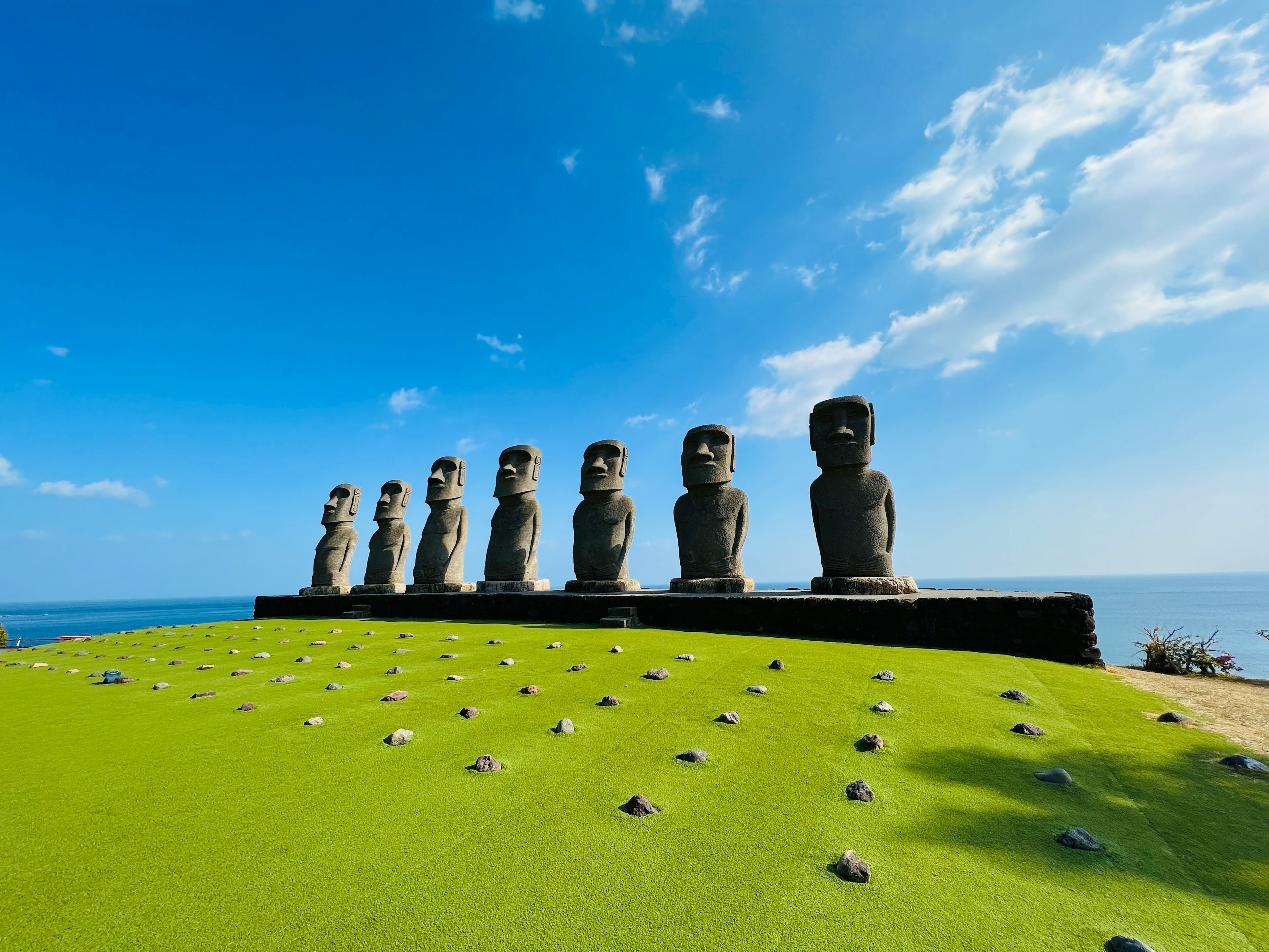 Una fila di statue Moai sull'isola di Pasqua sotto un cielo blu con erba verde