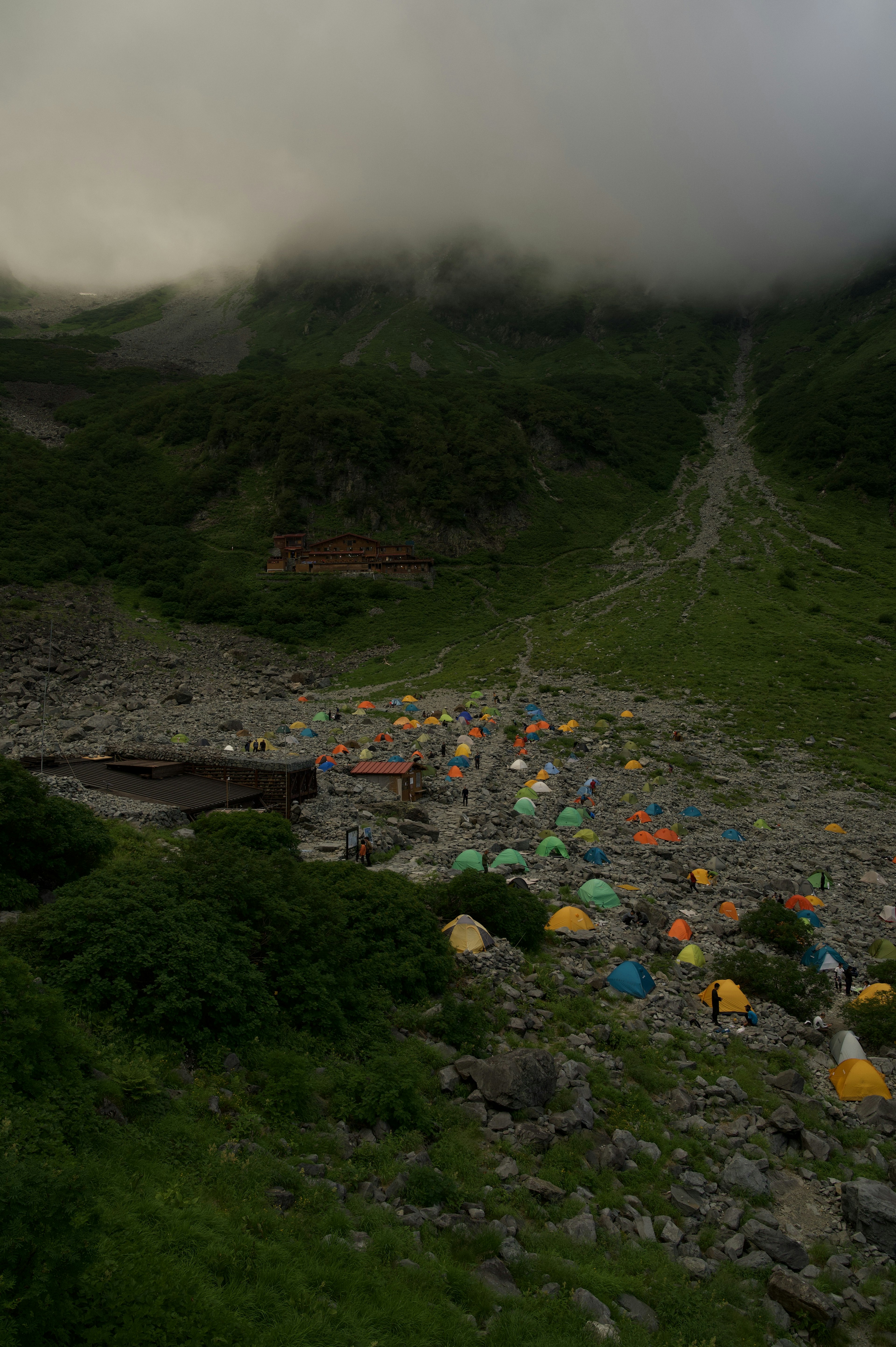 Colorful tents in a lush green valley surrounded by mountains and mist