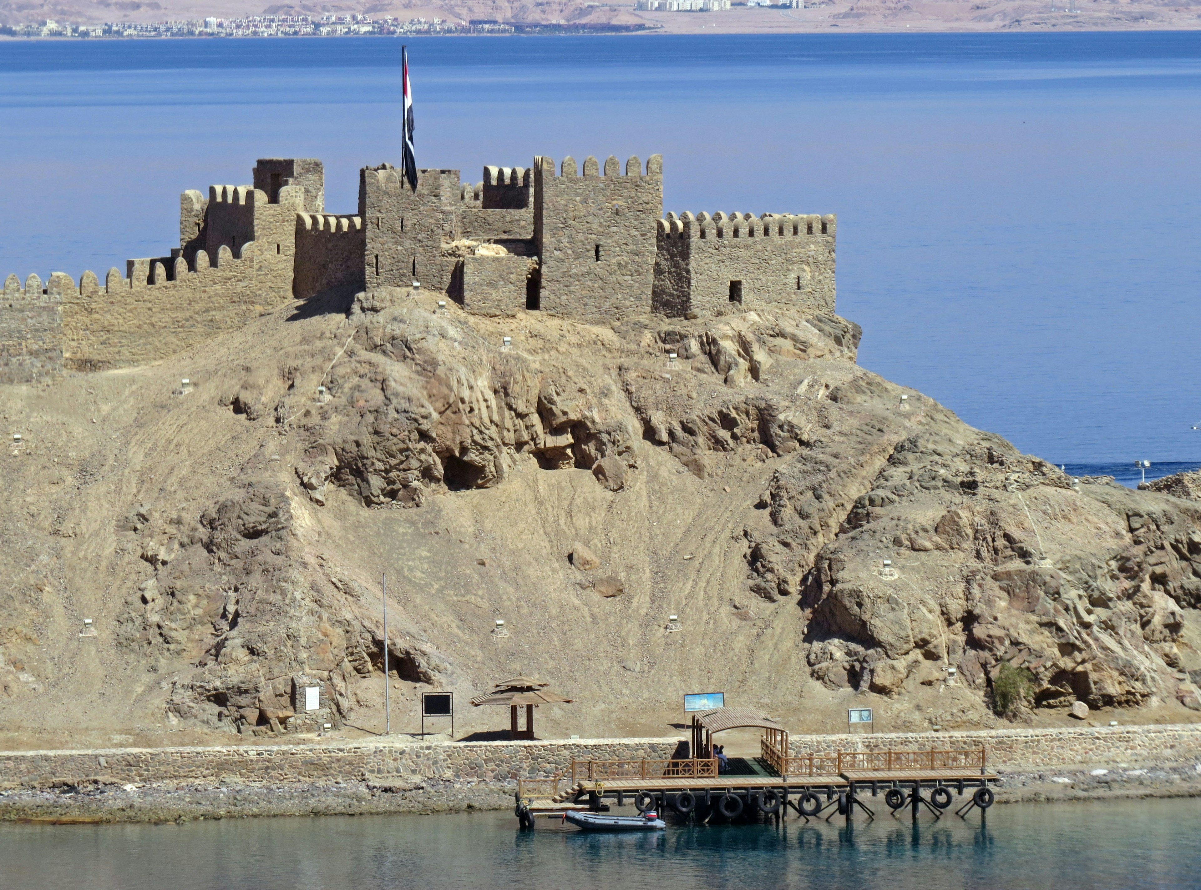 Un château historique entouré d'eau avec un terrain rocheux et un ciel bleu clair