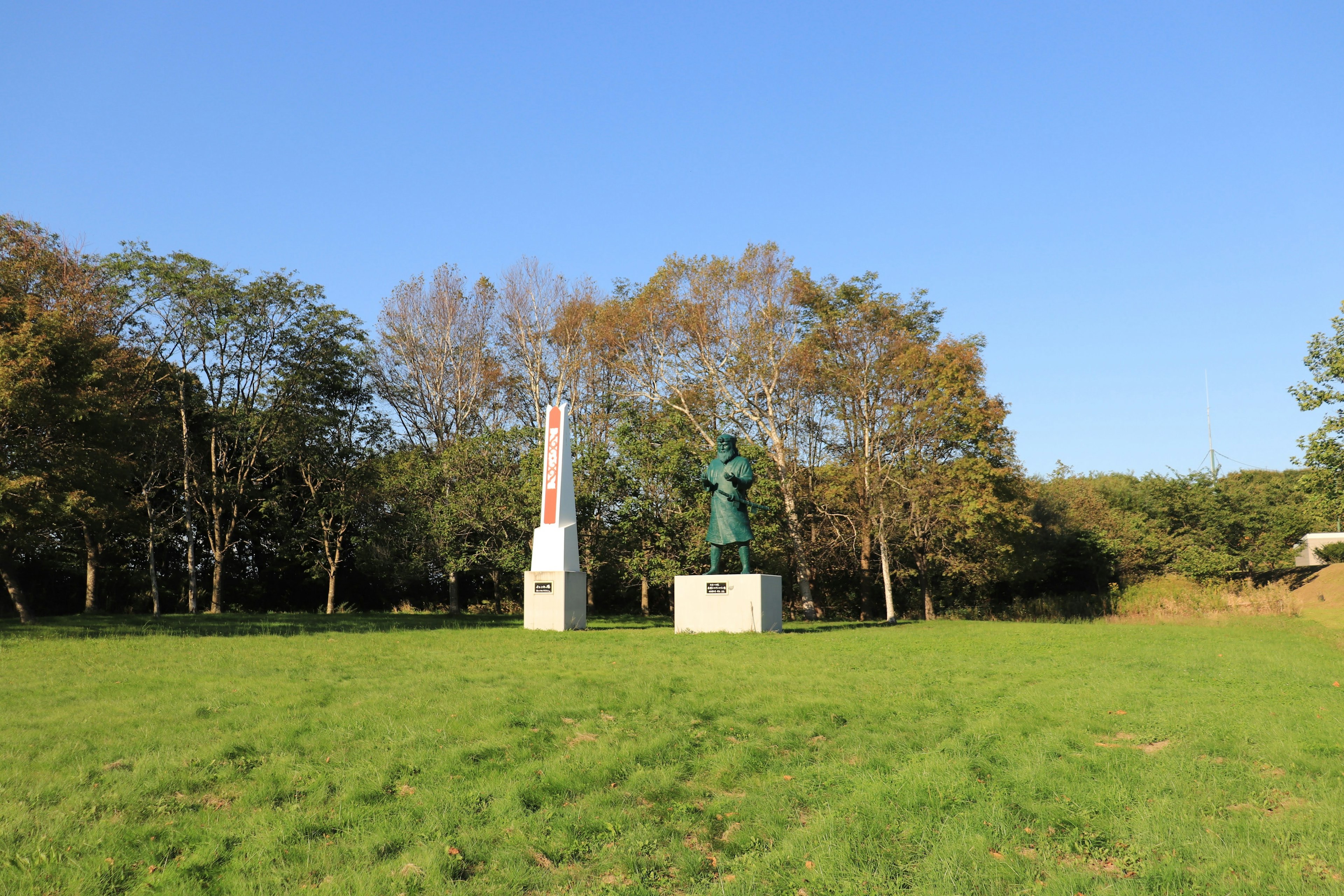 Due statue che si ergono in un prato verde sotto un cielo blu con alberi sullo sfondo