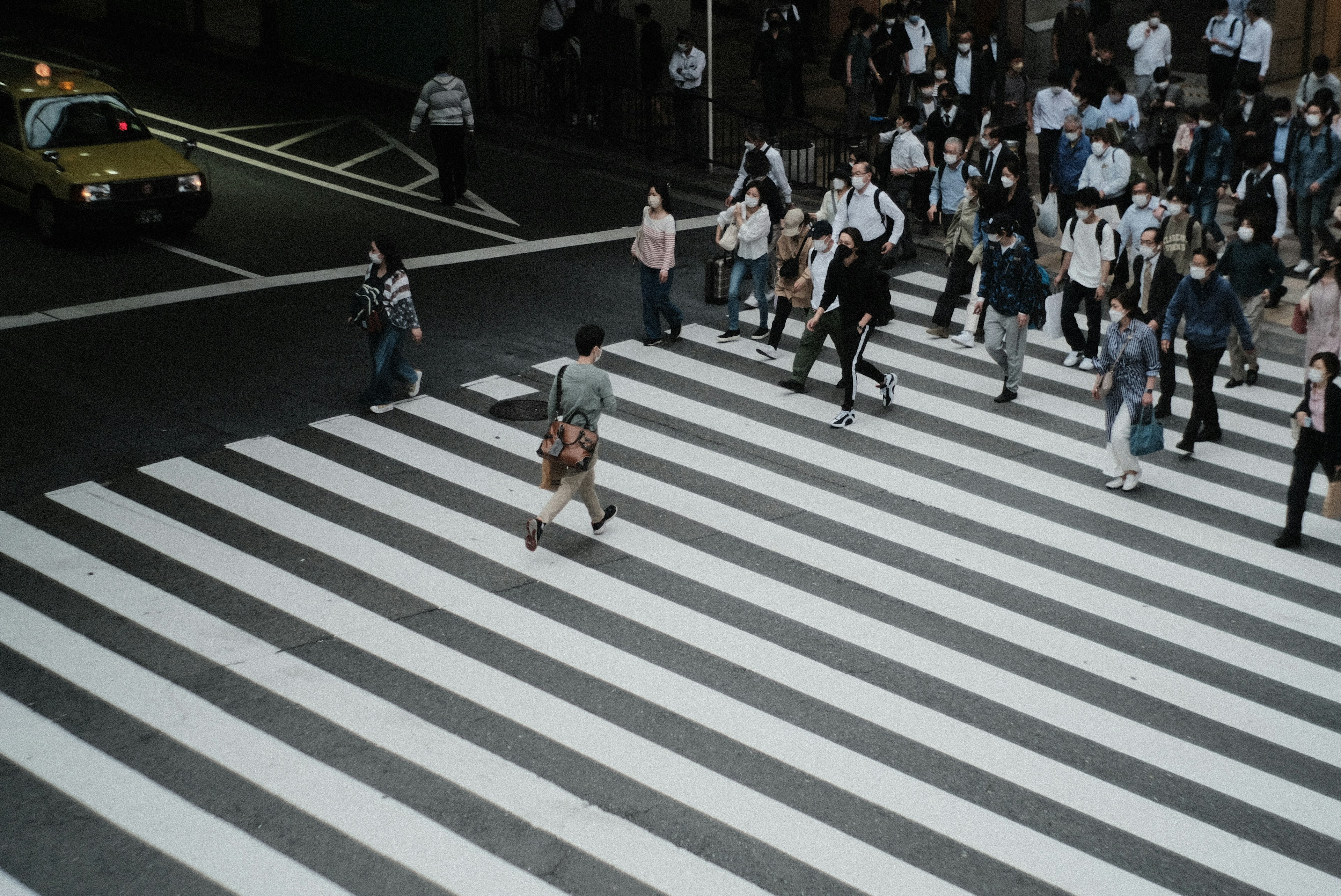 白い横断歩道を渡る人々の群れとタクシー