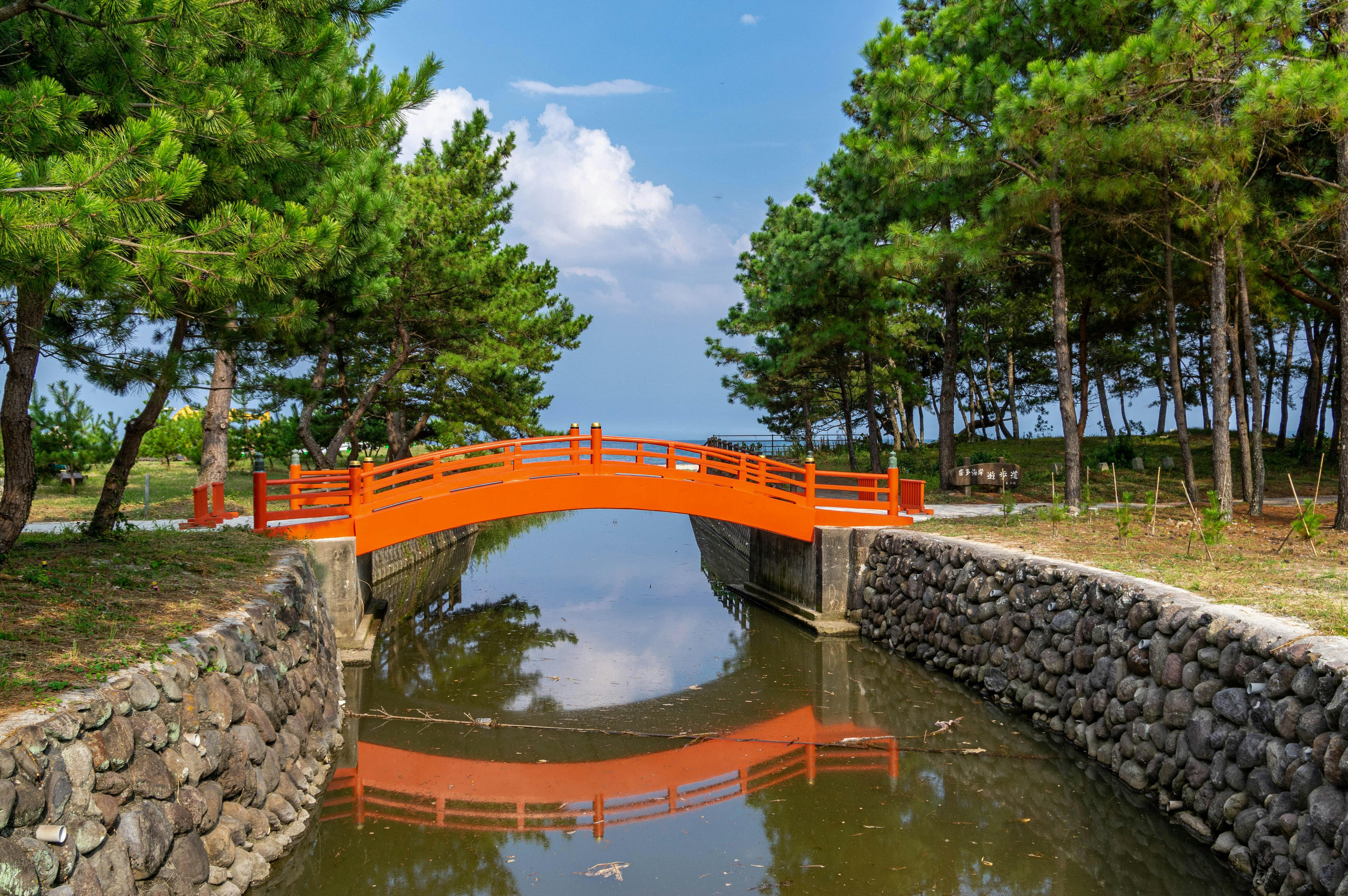 橙色の橋が水面に映る緑豊かな公園の風景